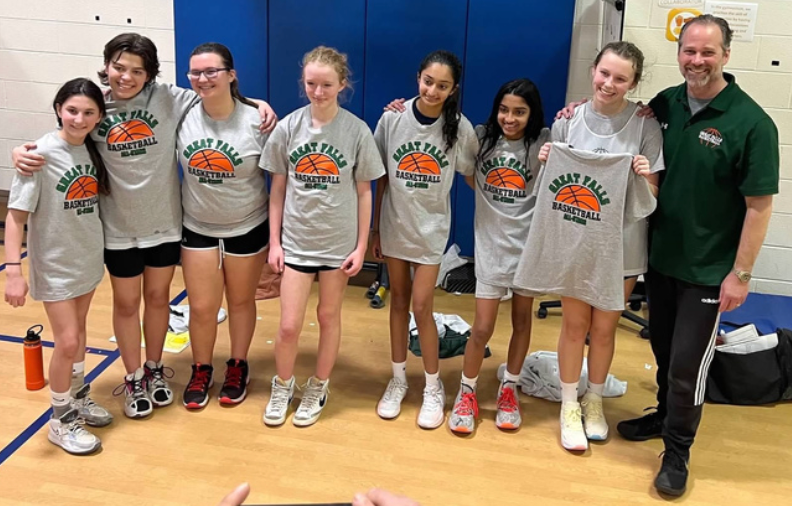Seven people pose indoors on a gym floor, wearing gray event T-shirts and holding a trophy.