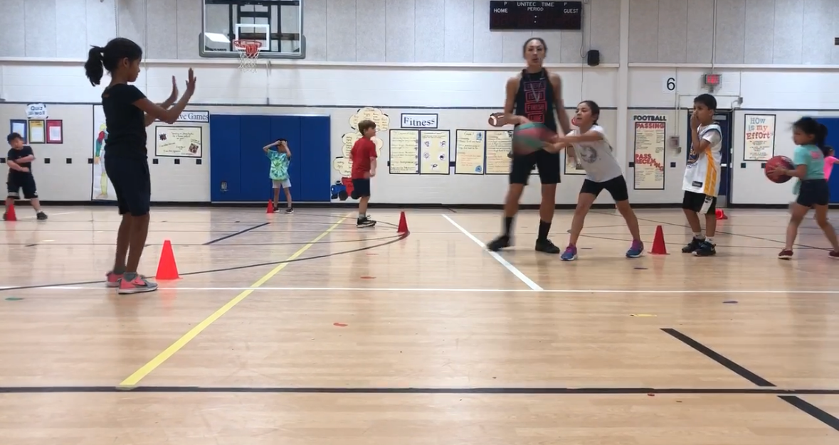 People practicing drills in a gymnasium with cones and a basketball hoop in the background