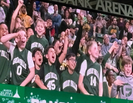 Cheering crowd in green jerseys at a sports arena, raising arms and celebrating behind a barrier