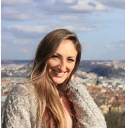 Smiling woman in a gray scarf with a cityscape and cloudy sky in the background