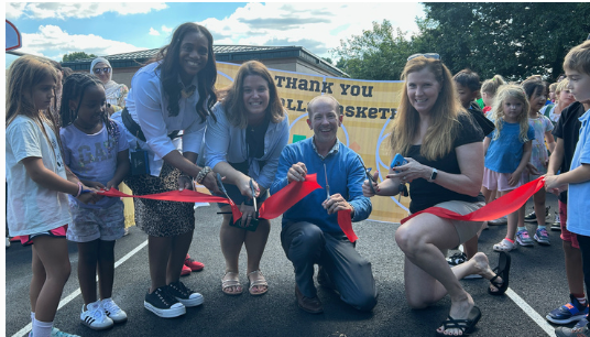 People cutting a red ribbon at a community event outdoors, with a thank-you banner in the background
