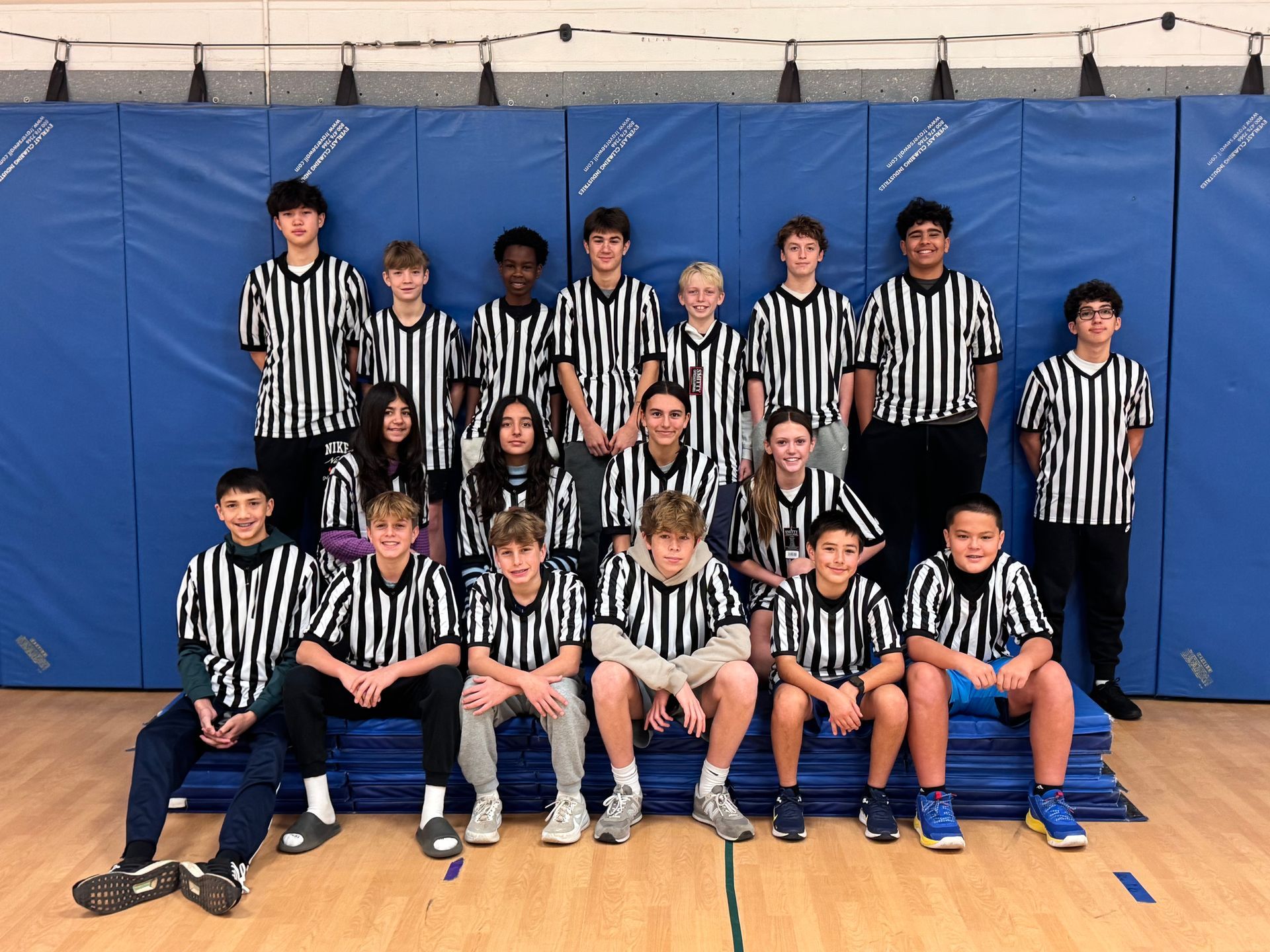 Youth sports team posing indoors in black-and-white striped jerseys in front of blue wall mats