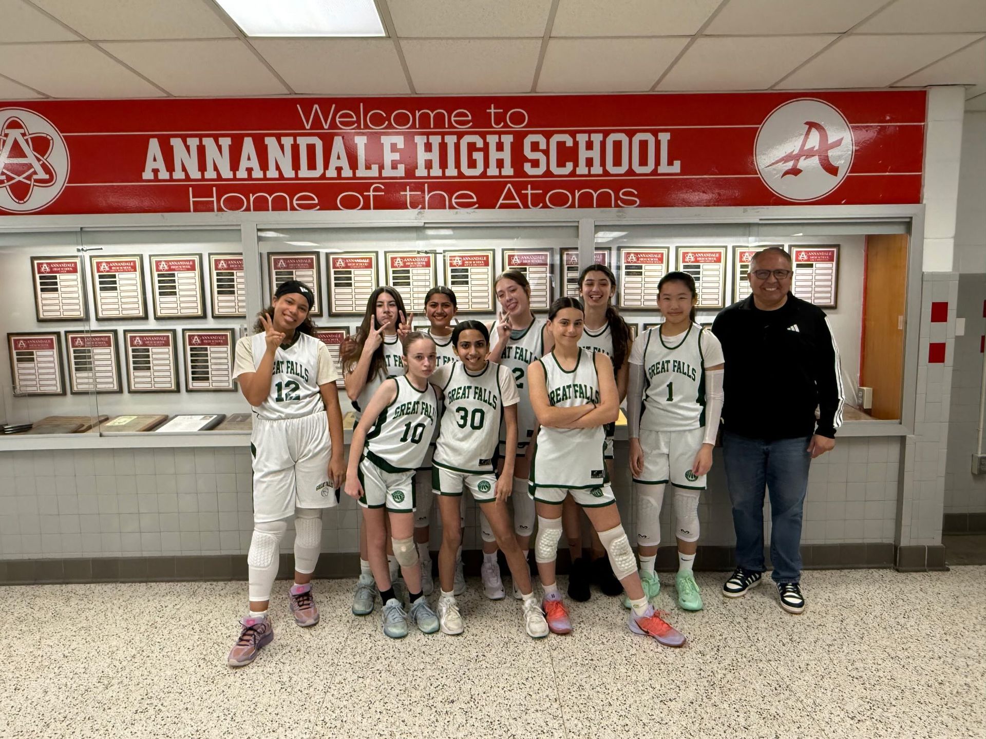 Basketball team posing in front of Annandale High School trophy wall with a coach.