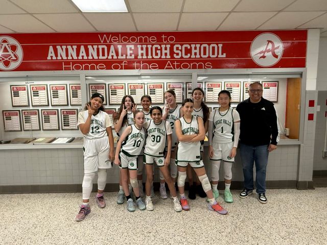Annandale High School basketball team posing in front of a trophy display, wearing white uniforms