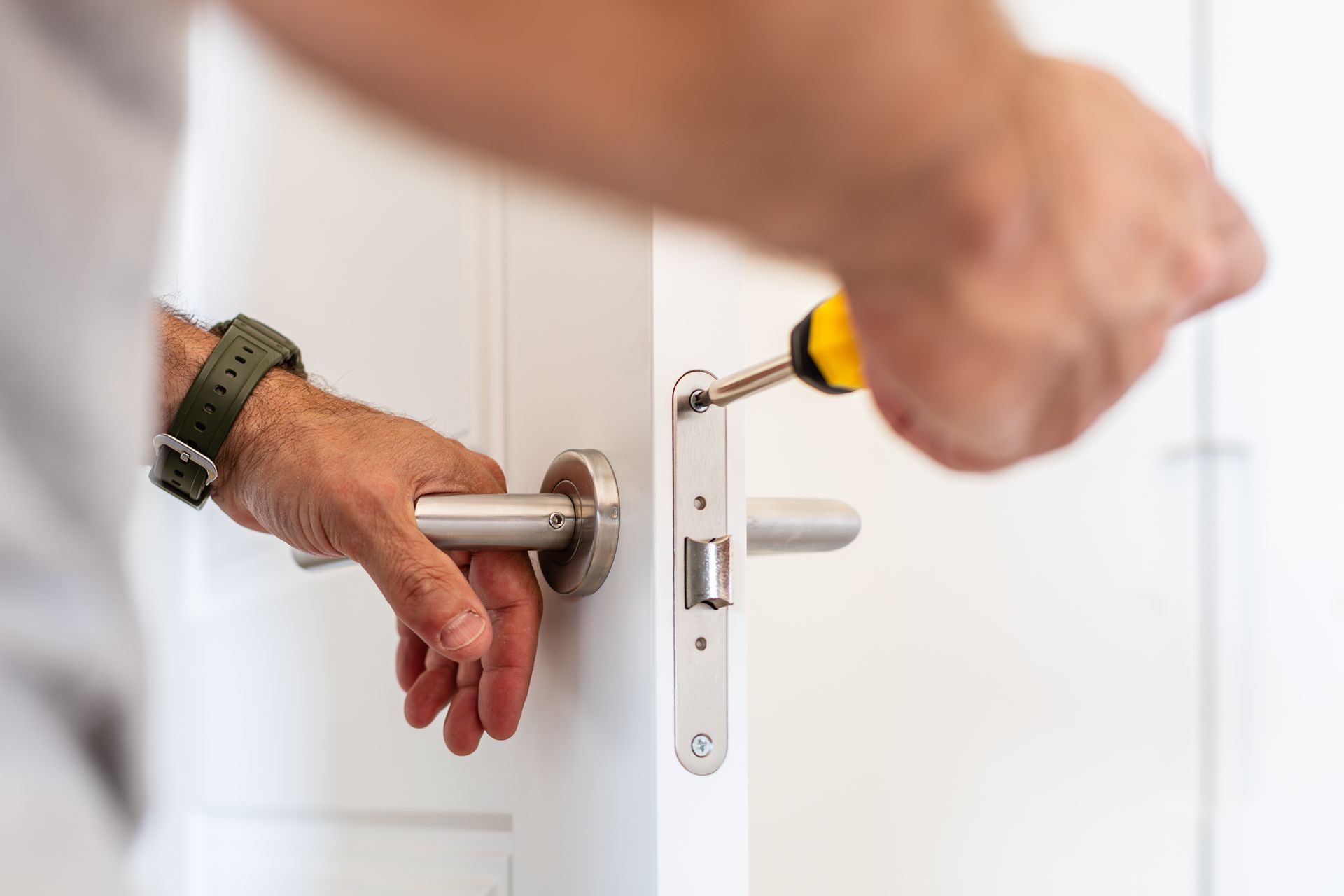 Close-up of a locksmith installing or repairing a door handle and lock mechanism using a screwdriver
