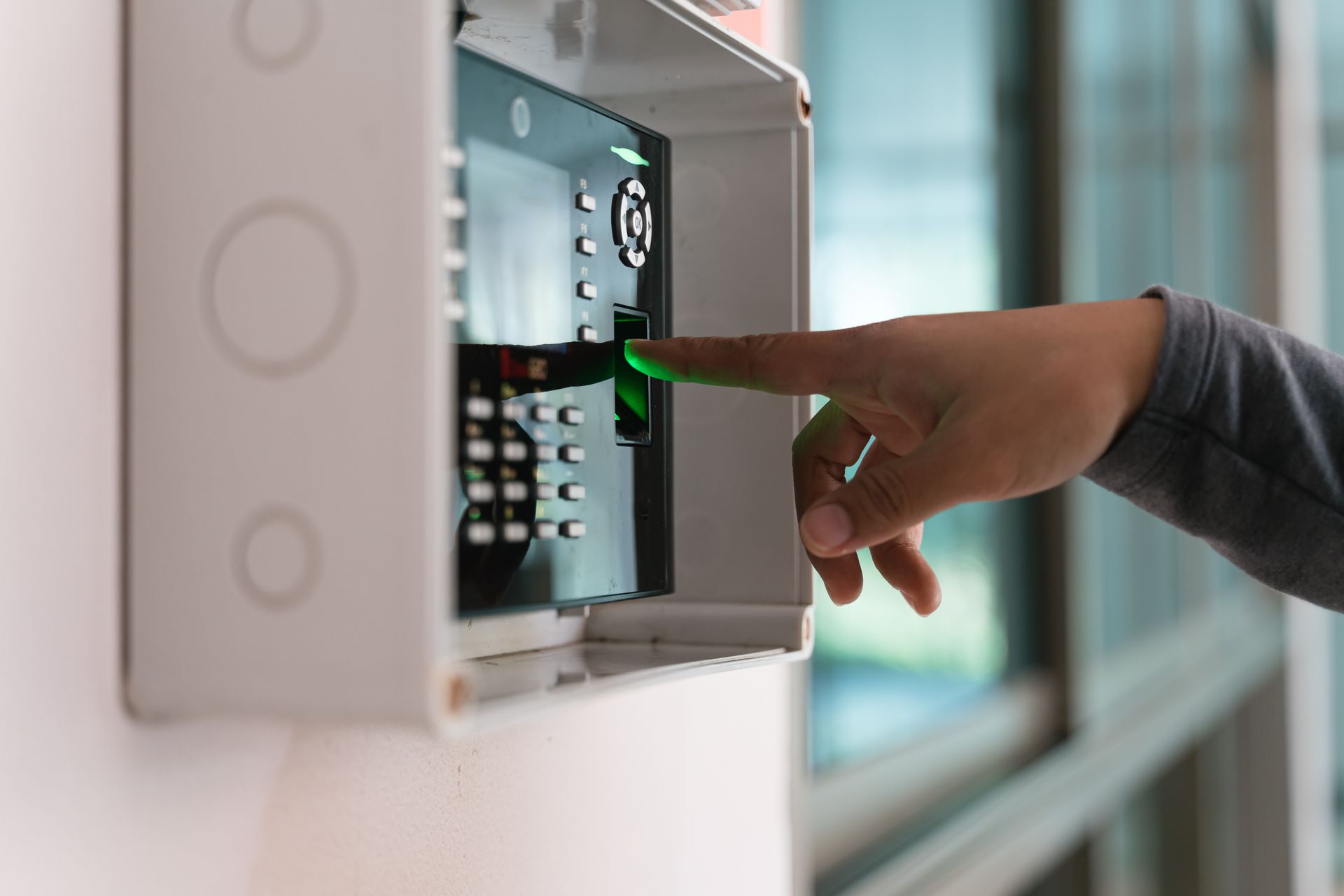 Finger pressing a fingerprint scanner on a keypad for secure access.