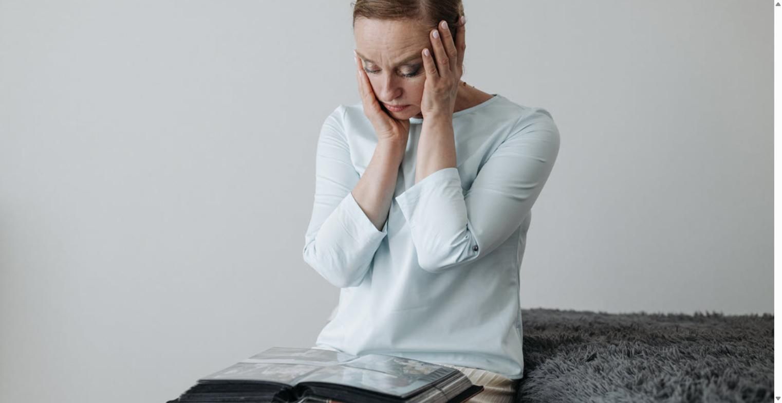 Worried woman resting her head in her hands while looking at an open photo album