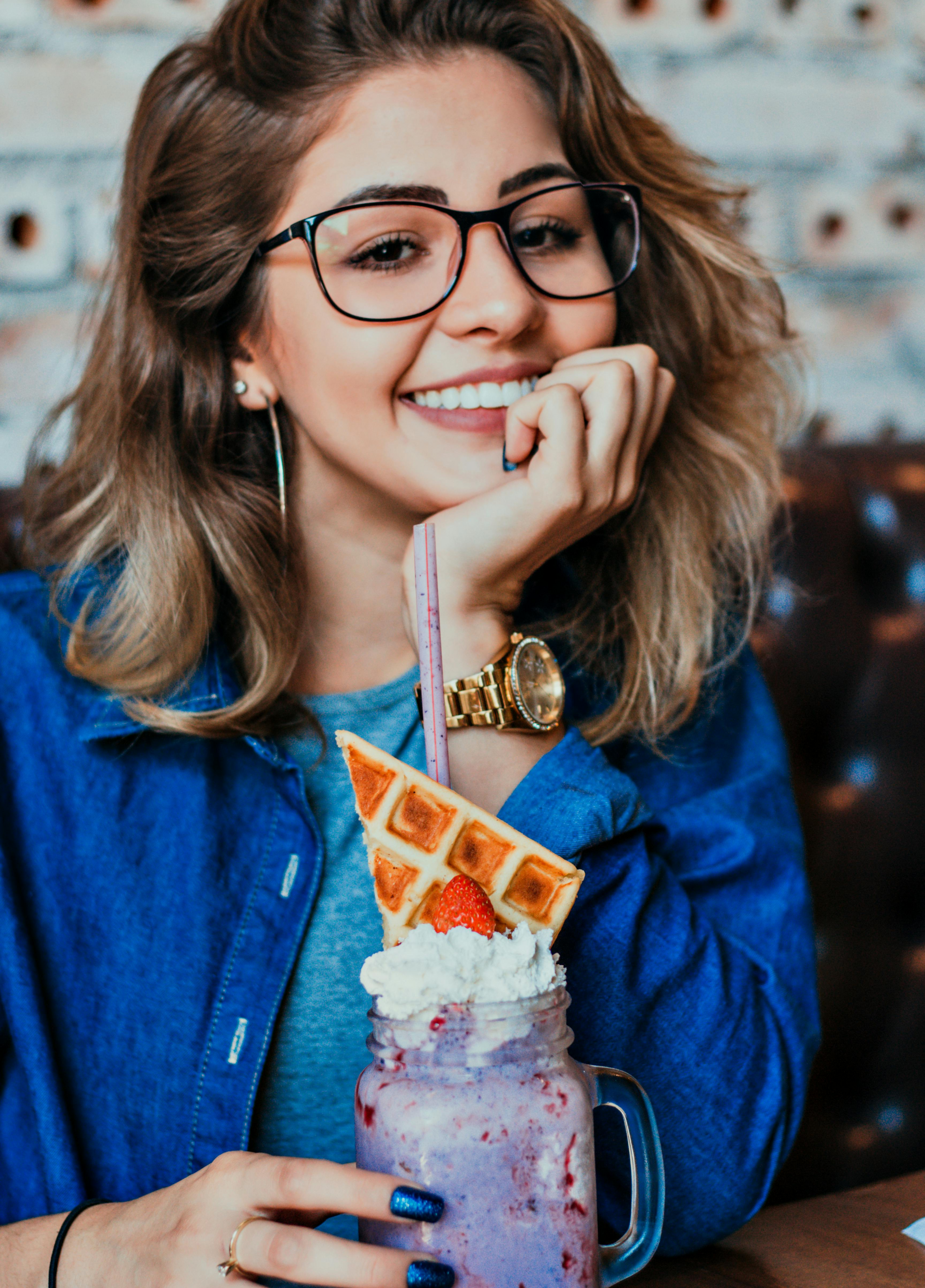 Woman in glasses smiling, holding a mason jar milkshake.