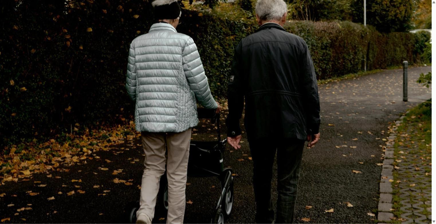 Elderly couple walking outdoors on an autumn path, one using a rolling walker