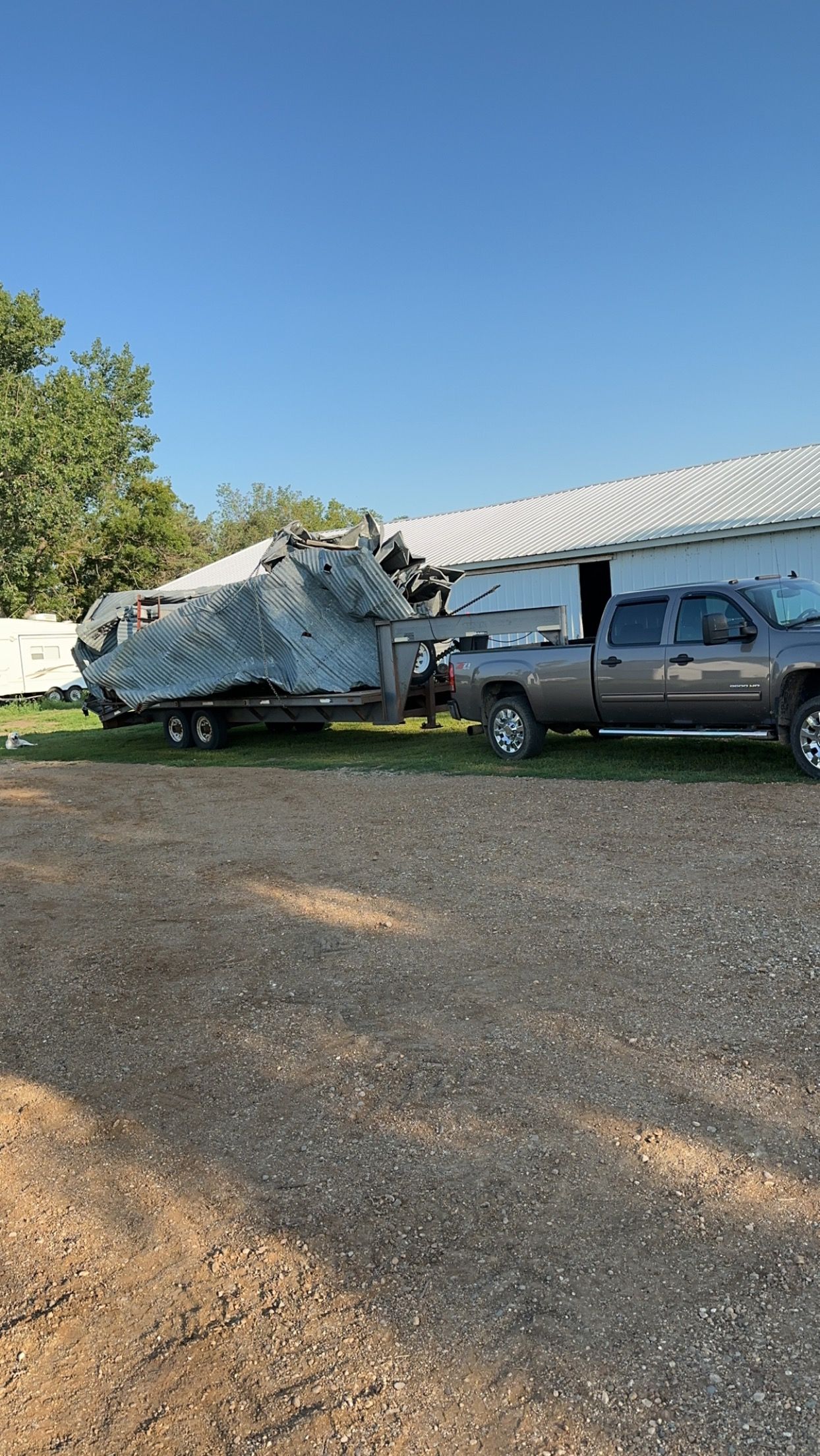 Gray pickup truck towing a trailer with a covered boat, parked outside a white building under a blue sky.