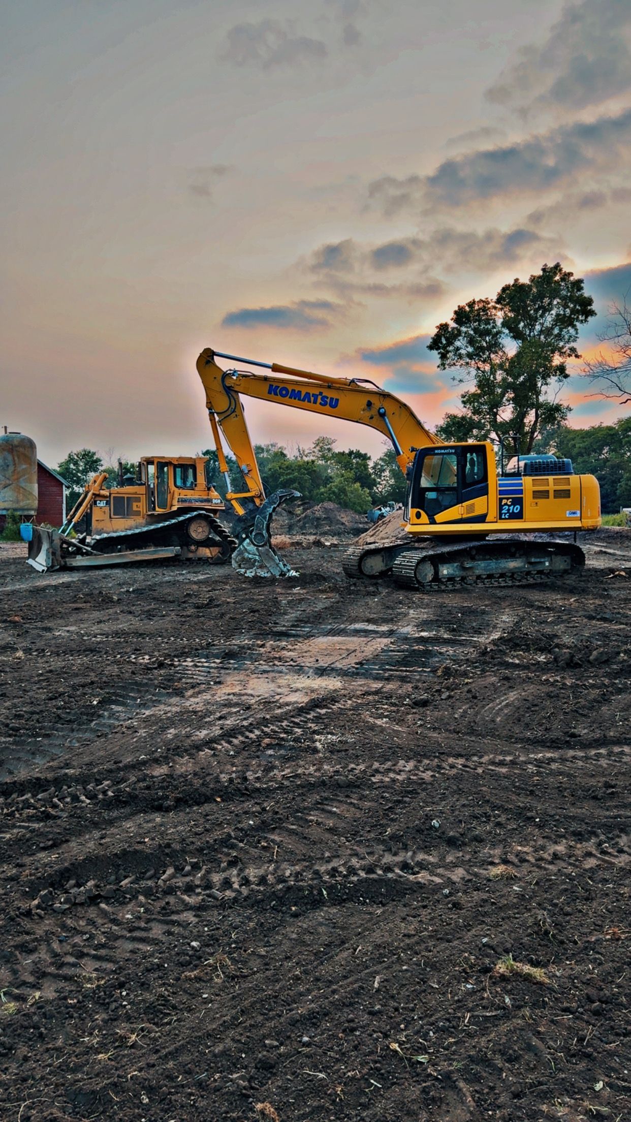 Two yellow construction vehicles on a muddy worksite under a cloudy sky.
