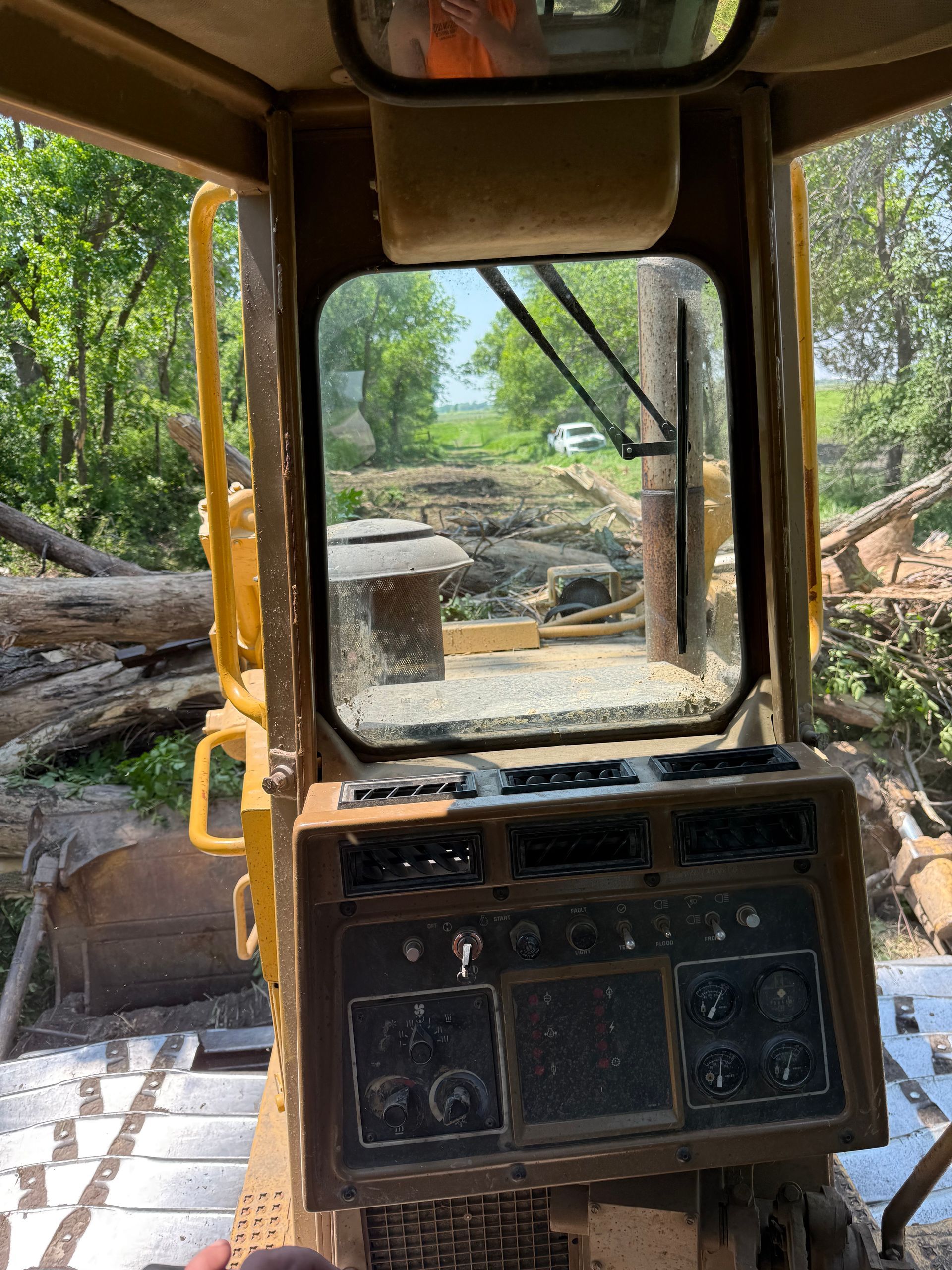 View from inside a yellow bulldozer cab, looking out at a work site with logs.