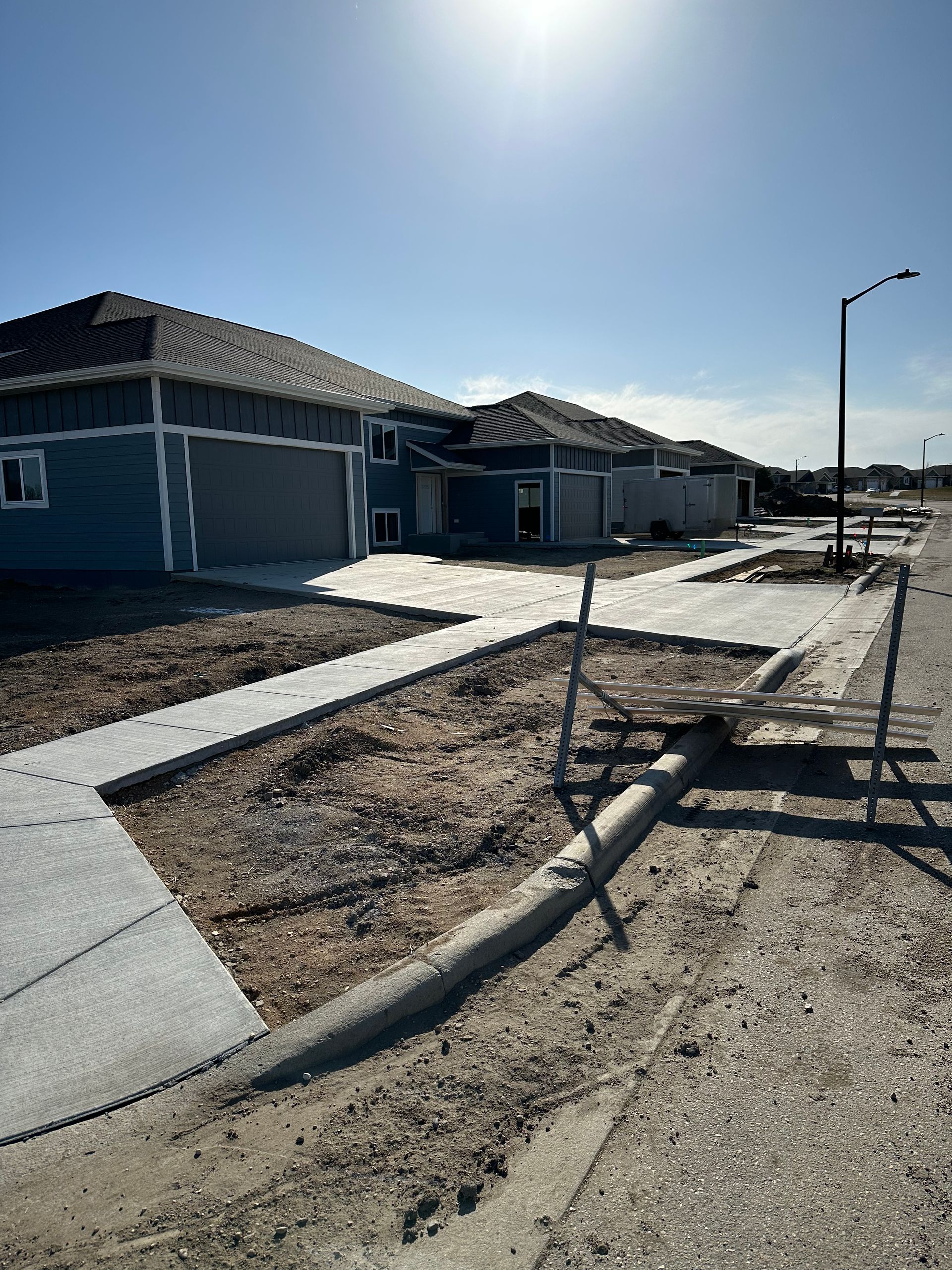 New houses under construction with sidewalks and street. Blue siding, sunny sky.