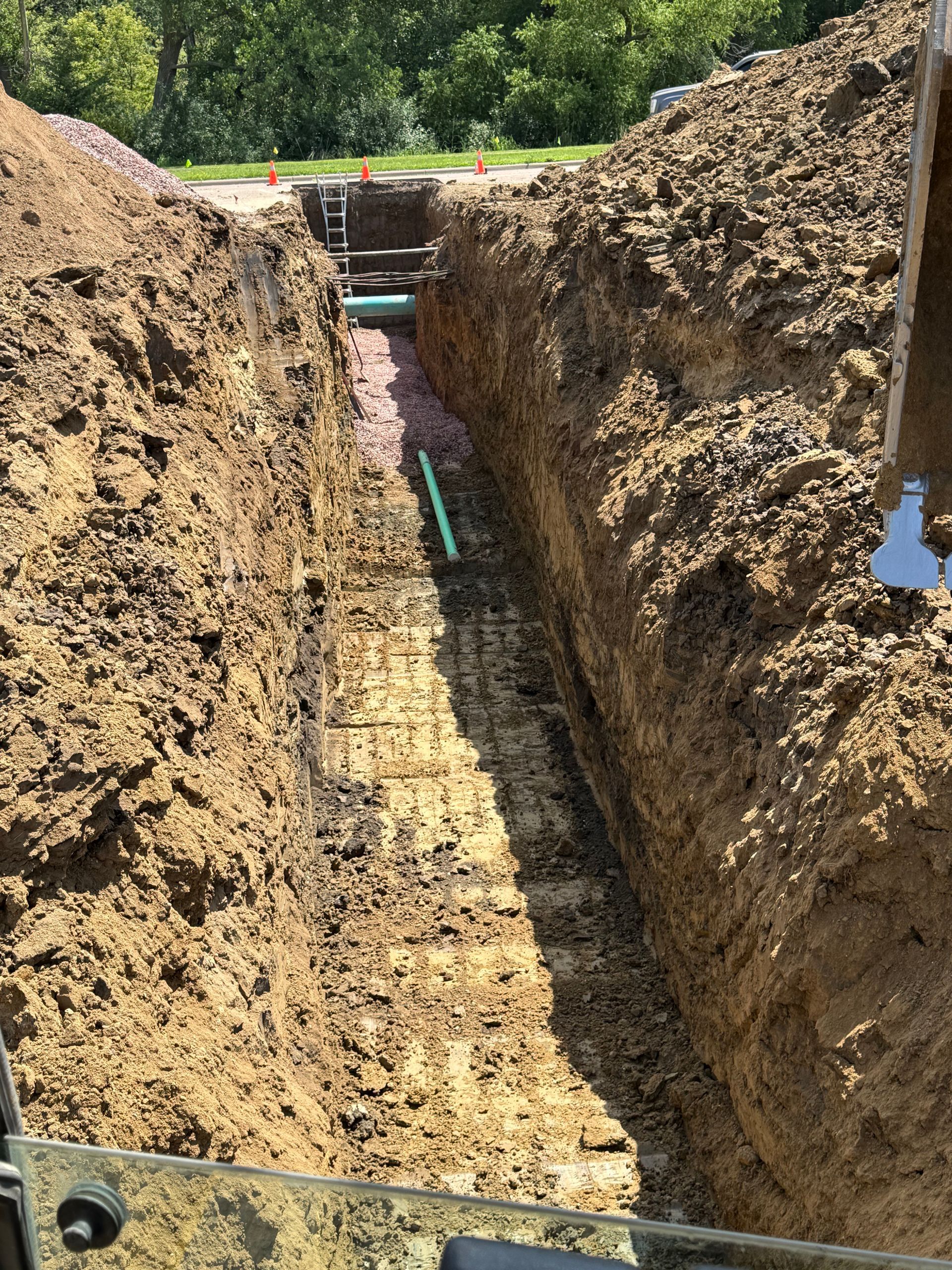 Trench dug in soil, containing green pipes. Construction site, outdoors.