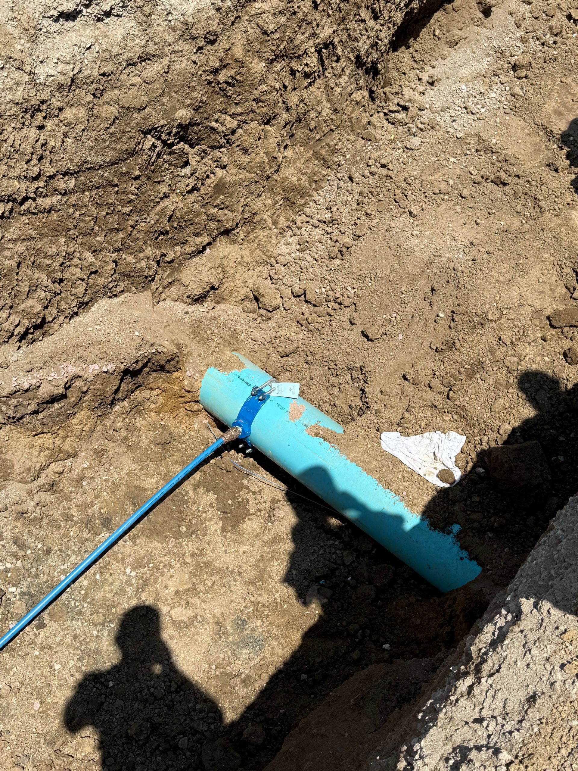 Blue PVC pipe in a dirt trench, with a connected blue wire.