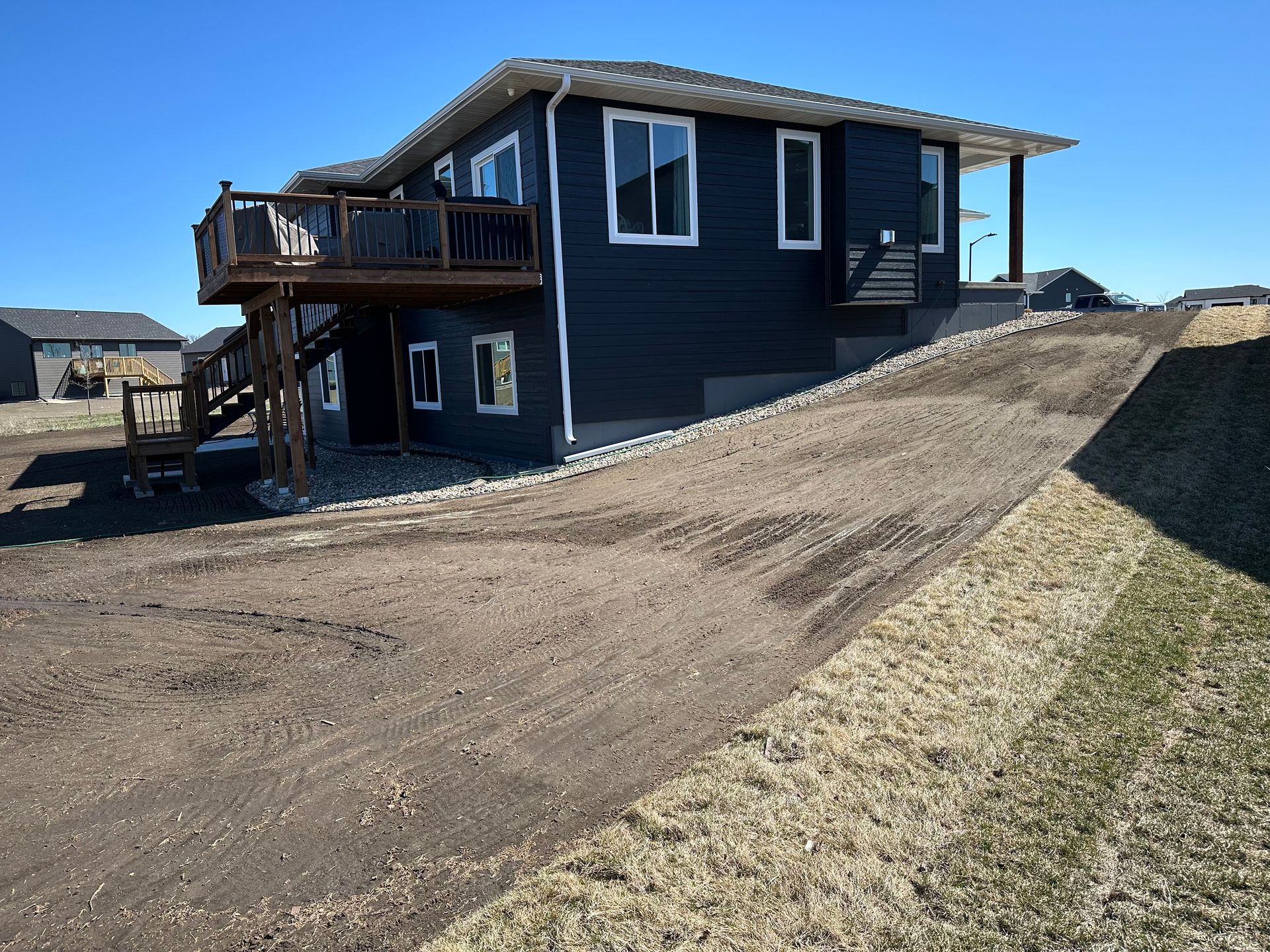Dark blue house with a gravel driveway and wooden deck on a sunny day.