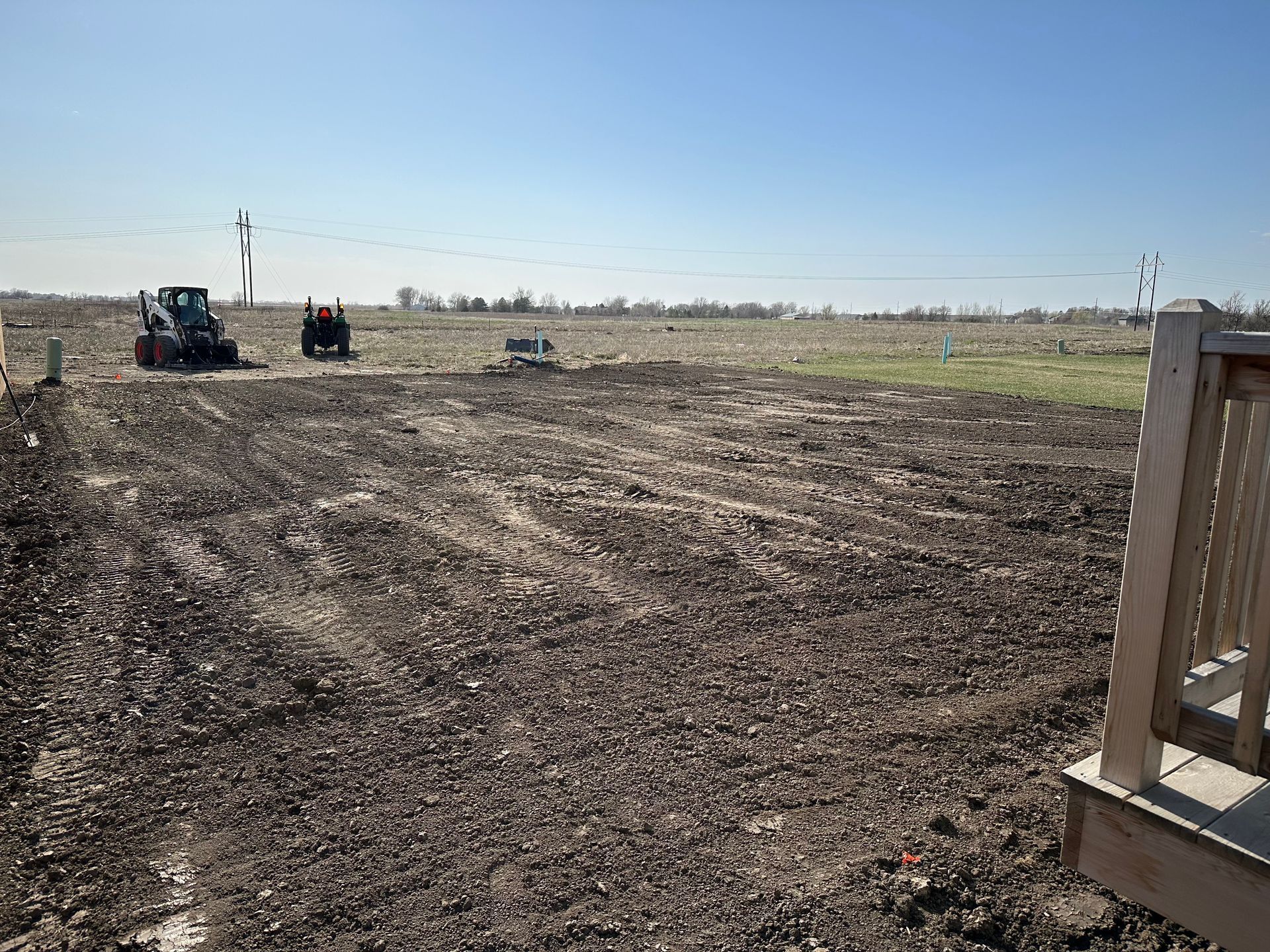 Dirt field being prepared for construction, with two small tractors. Sunny, clear sky.