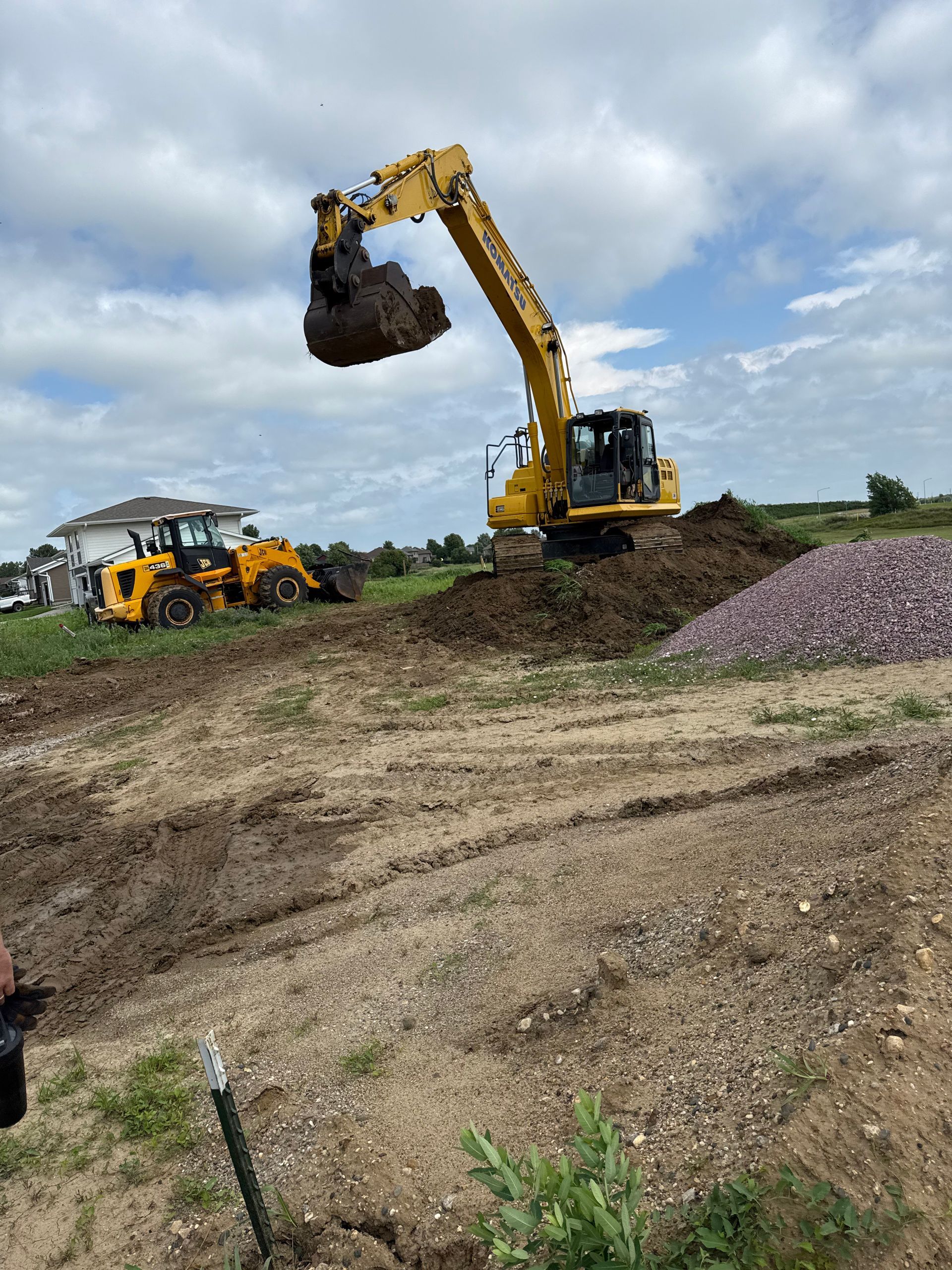 Yellow excavator lifting dirt, alongside a bulldozer on a construction site under cloudy sky.