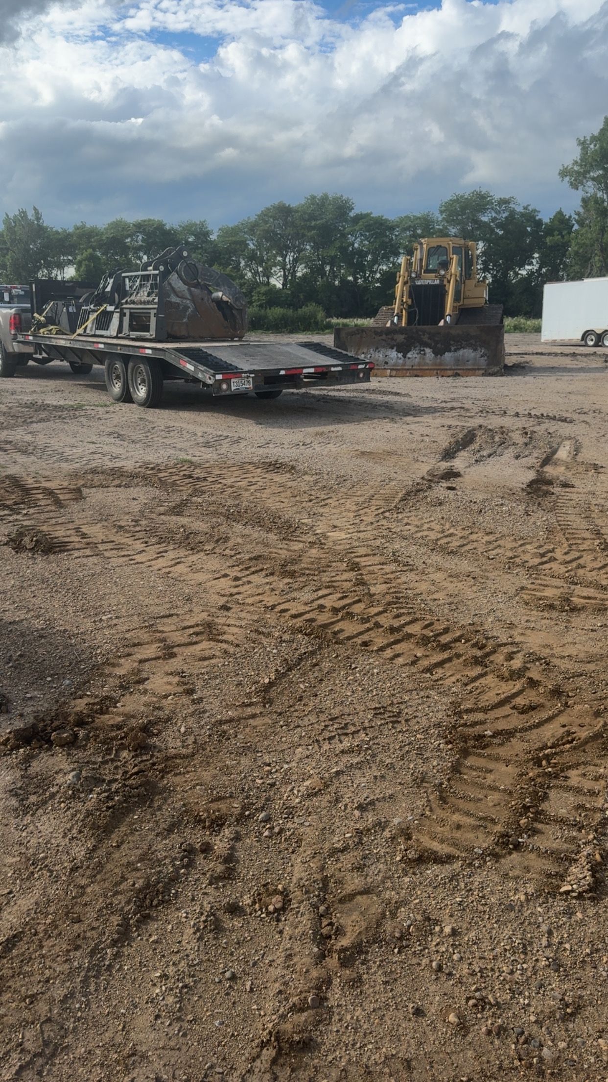 Construction site with heavy machinery, including a bulldozer and trailer, under a cloudy sky.