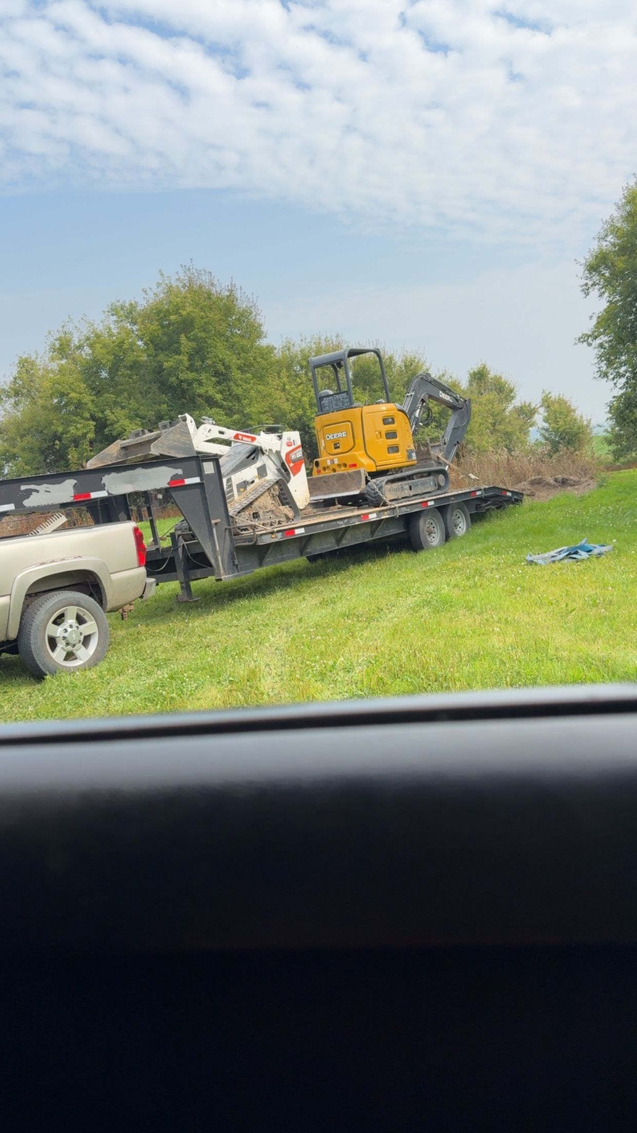 Truck pulling a trailer loaded with debris and a yellow excavator on a grassy field under a cloudy sky.