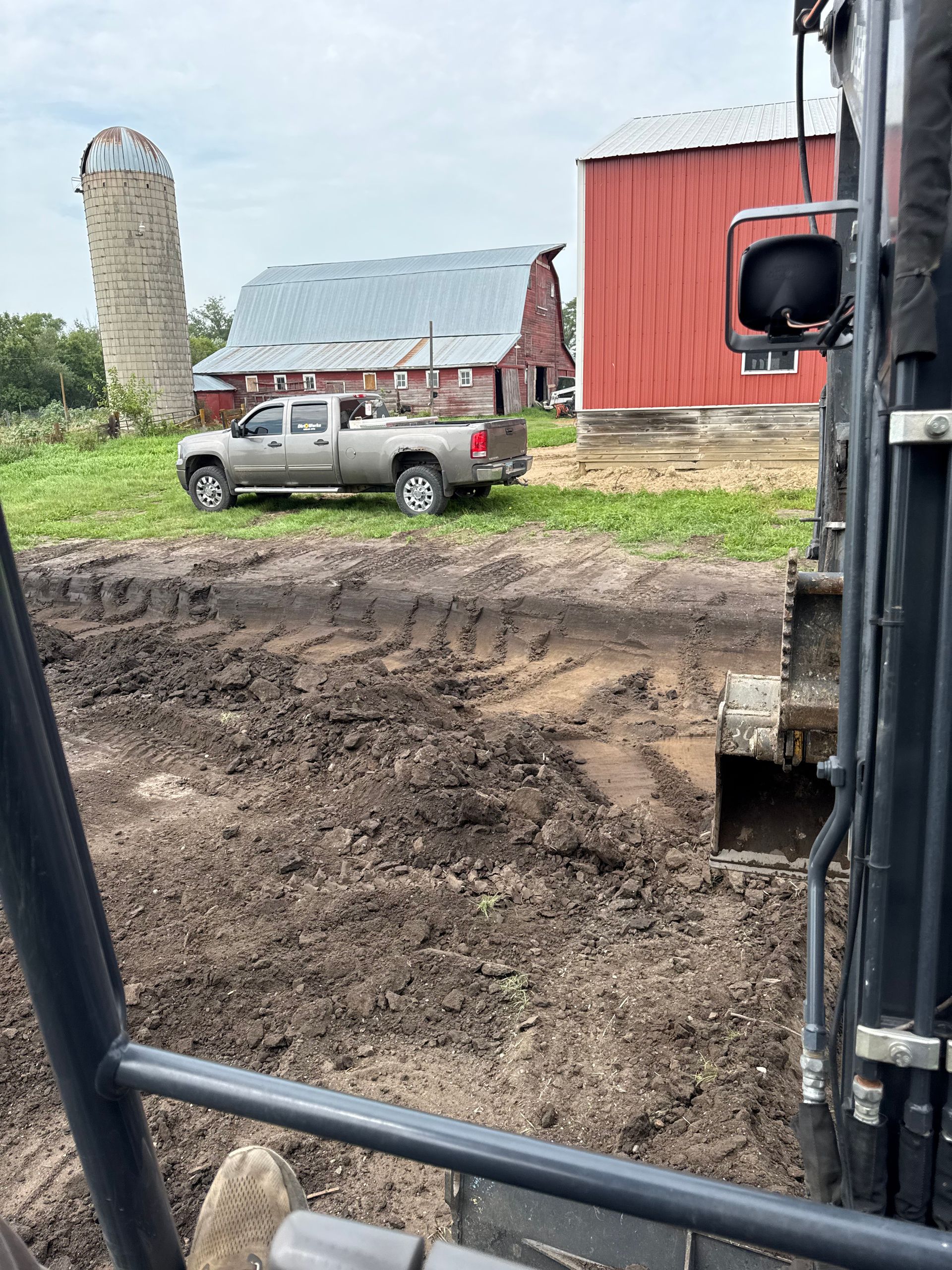 Muddy ground with a view of a farm, truck, silo, and red barn.