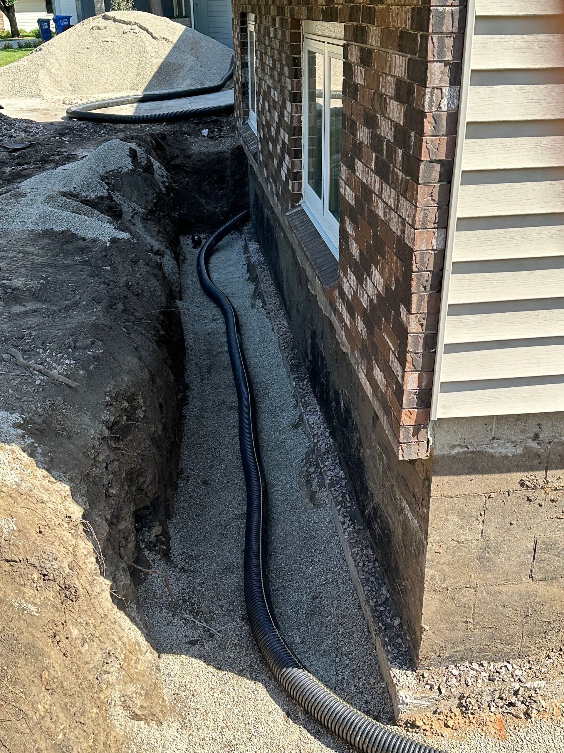 Trench dug along a house foundation, filled with gravel and black drainage pipe.