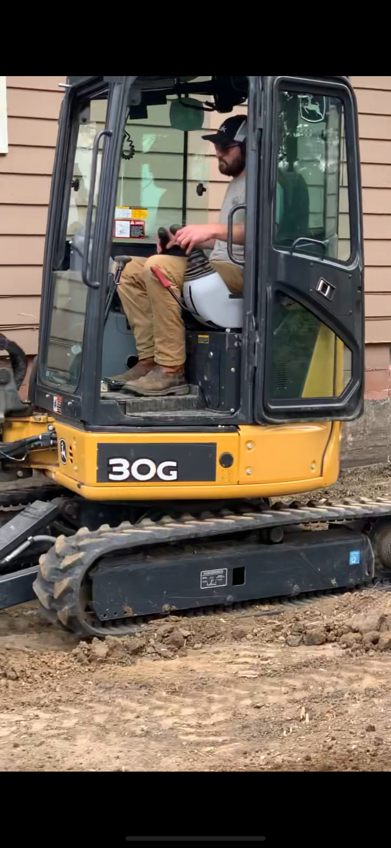 A person operating a yellow and black 30G excavator. They are wearing a cap and brown pants.