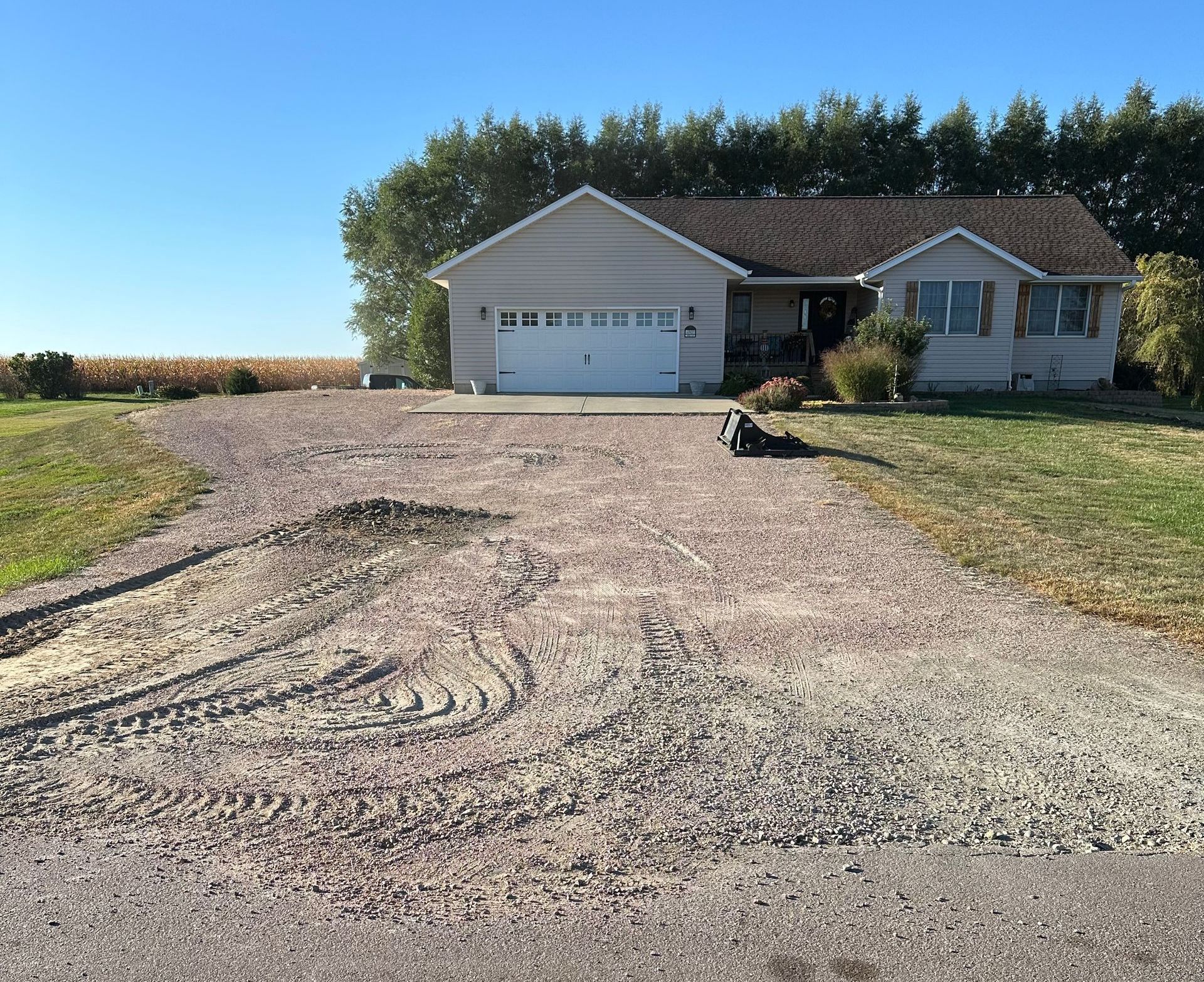 Gravel driveway leading to a one-story house with a white garage door, set in a rural landscape.