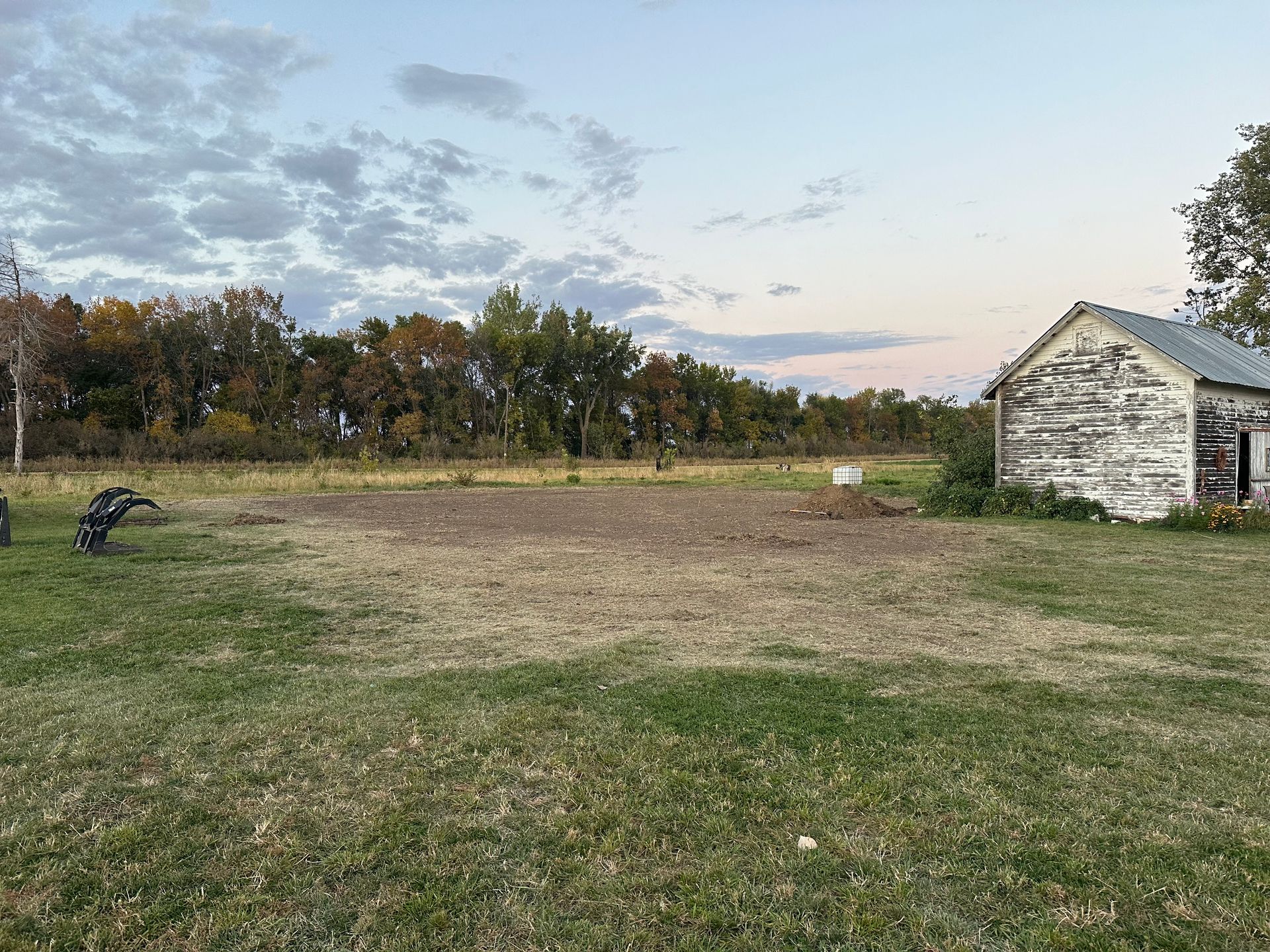 Grassy yard with a small, weathered shed, a bare patch of earth, and trees under a cloudy sky.