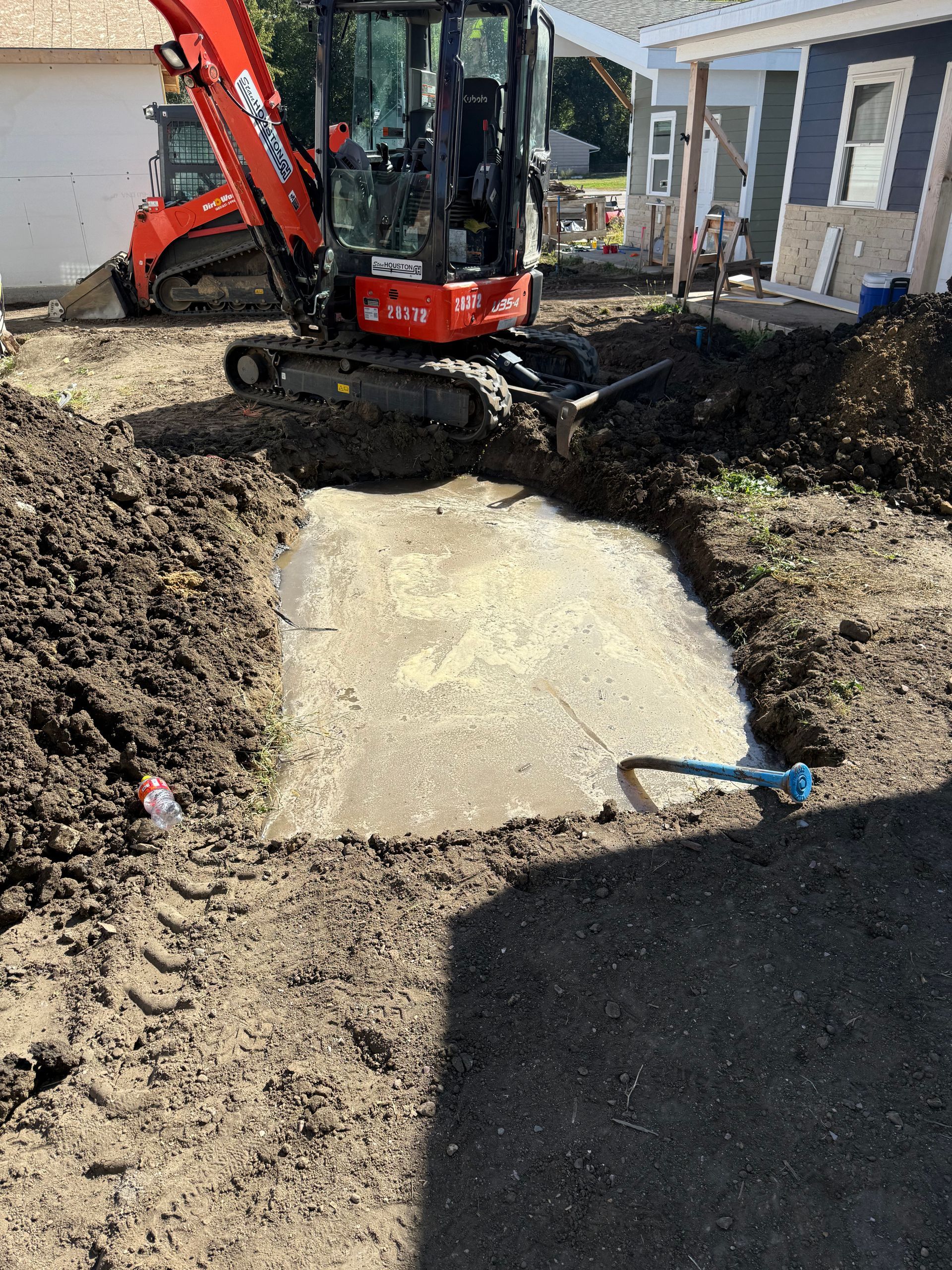 Mini excavator digging around a concrete pad in a yard.
