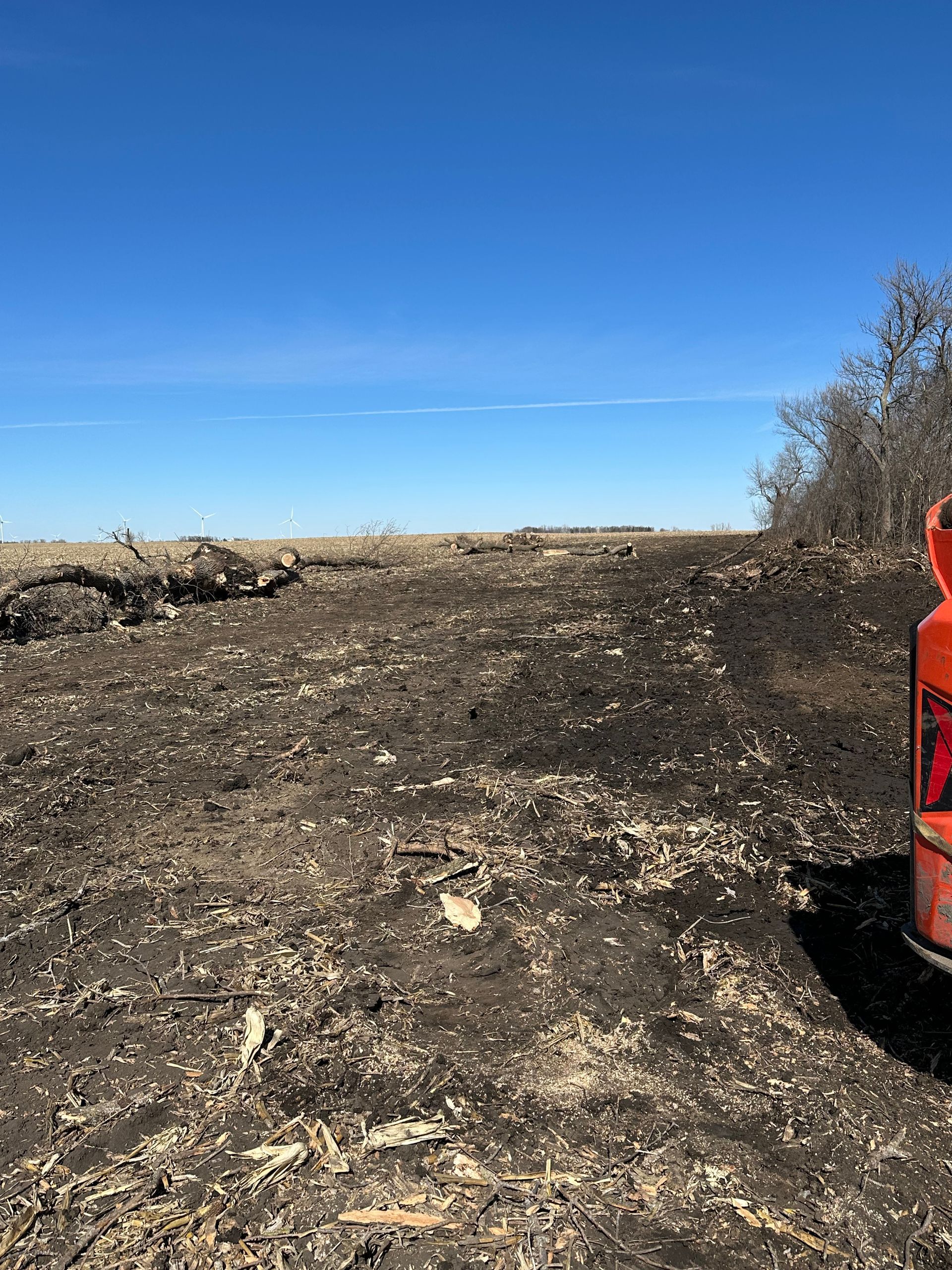A field of dark, charred earth under a bright blue sky, with a partial view of an orange object.