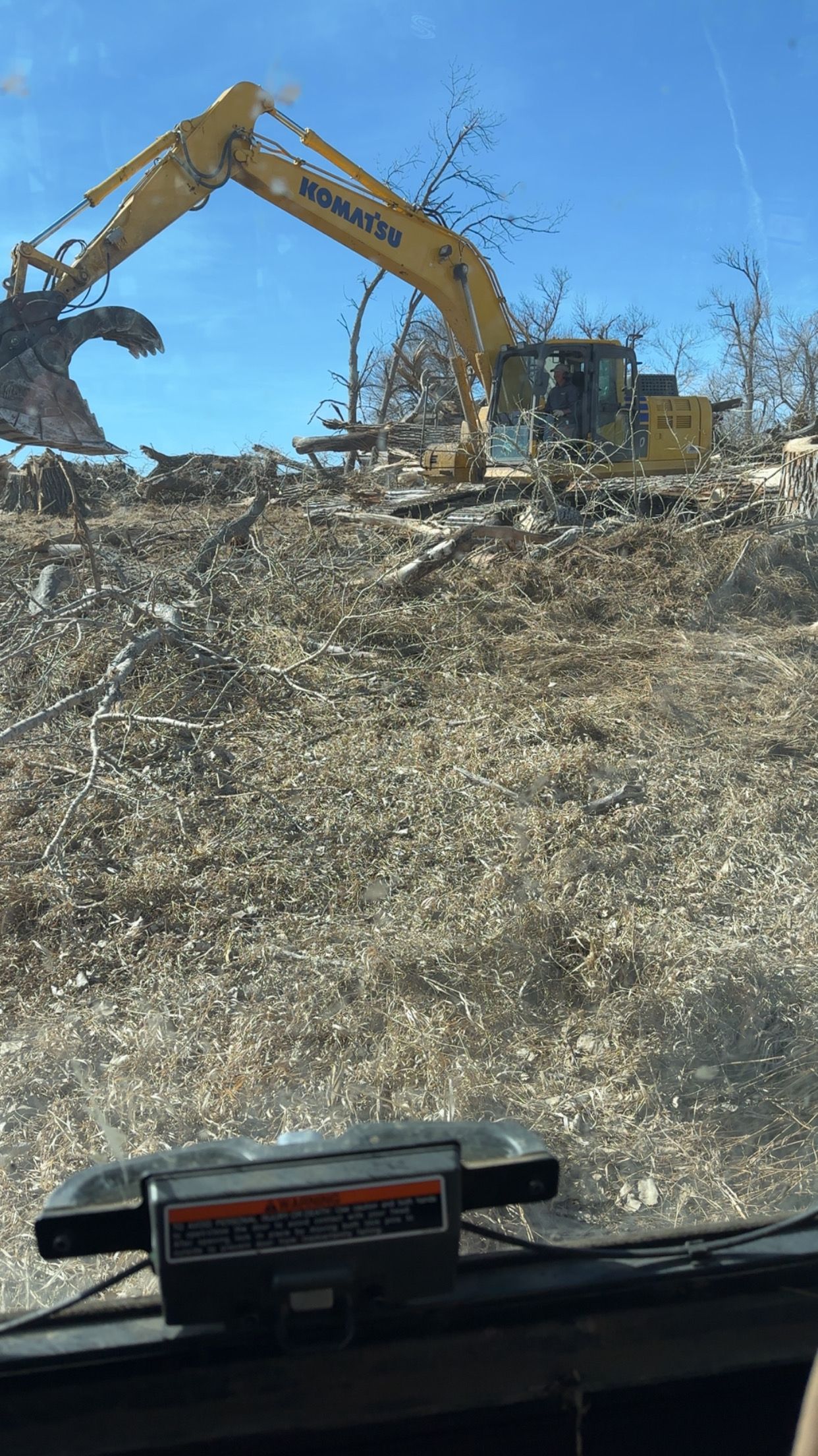 Yellow excavator clearing brush on a sunny day.