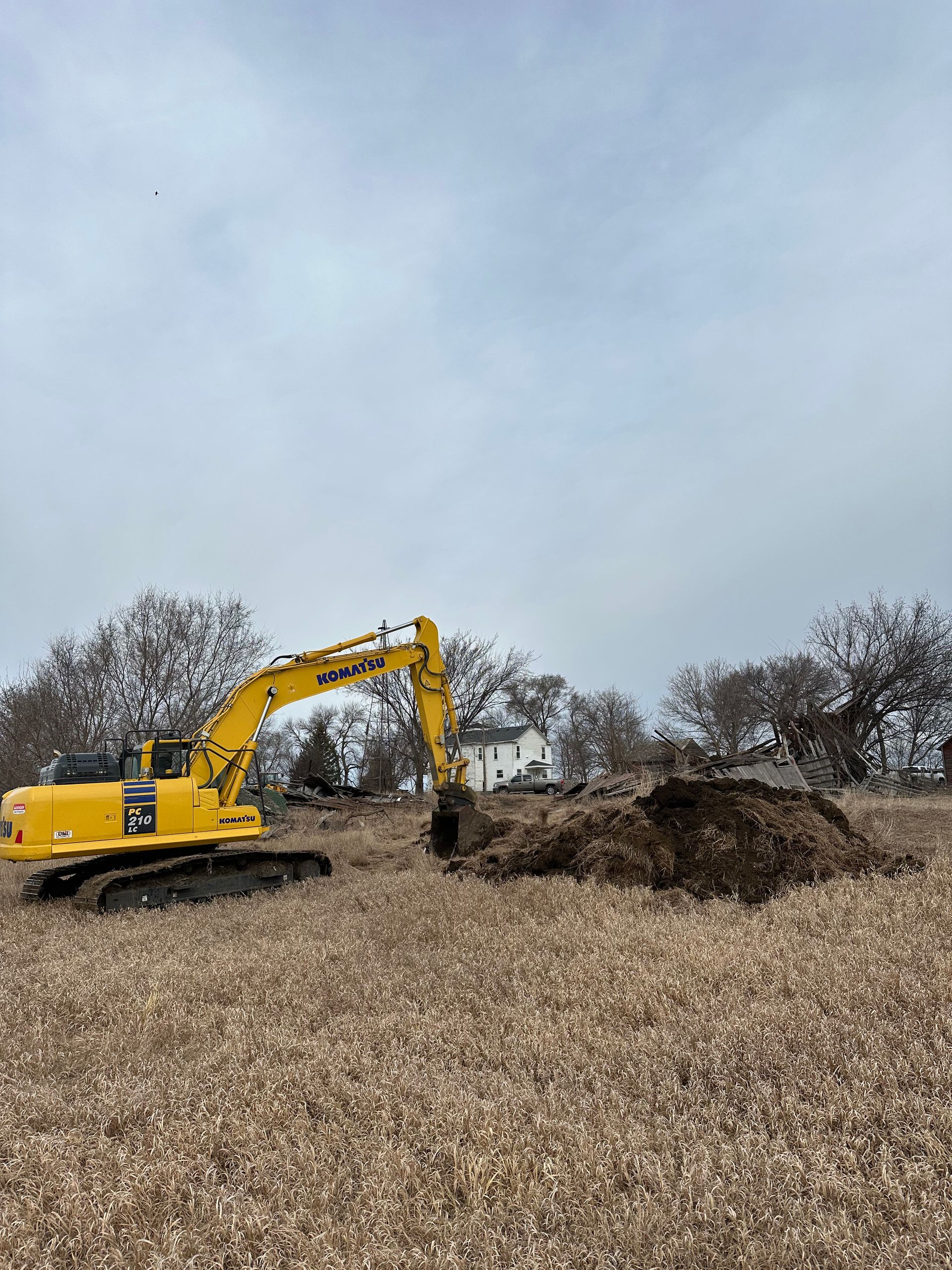 A yellow excavator digs a pile of dark earth in a field on an overcast day.