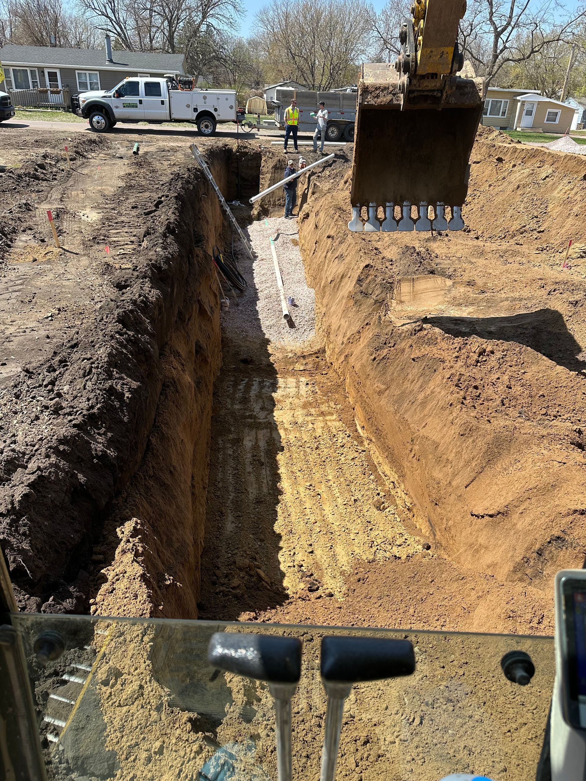 Excavator digging a trench for underground infrastructure; workers and truck in the background.