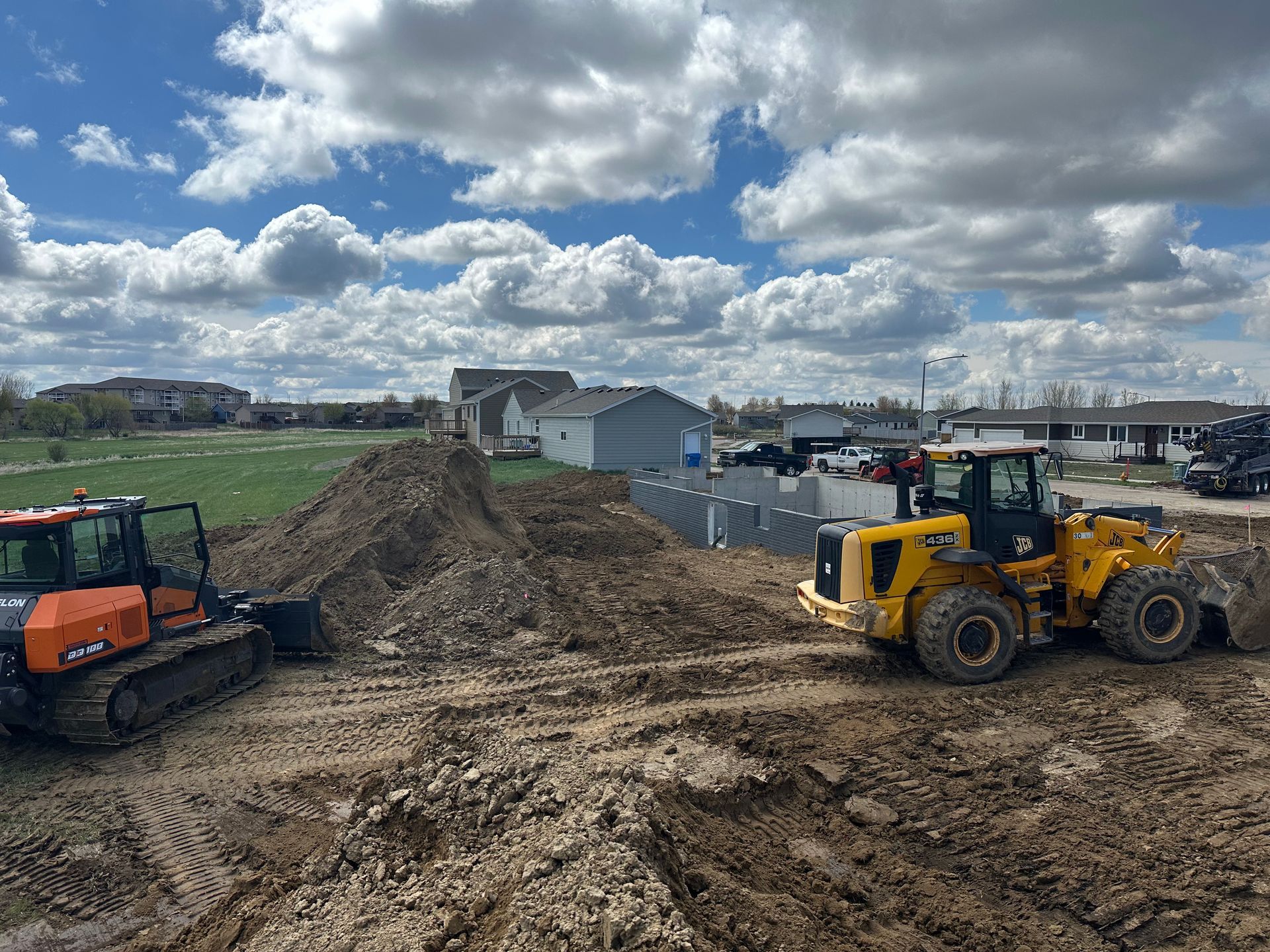 Two construction vehicles moving dirt on a muddy construction site under a cloudy sky.