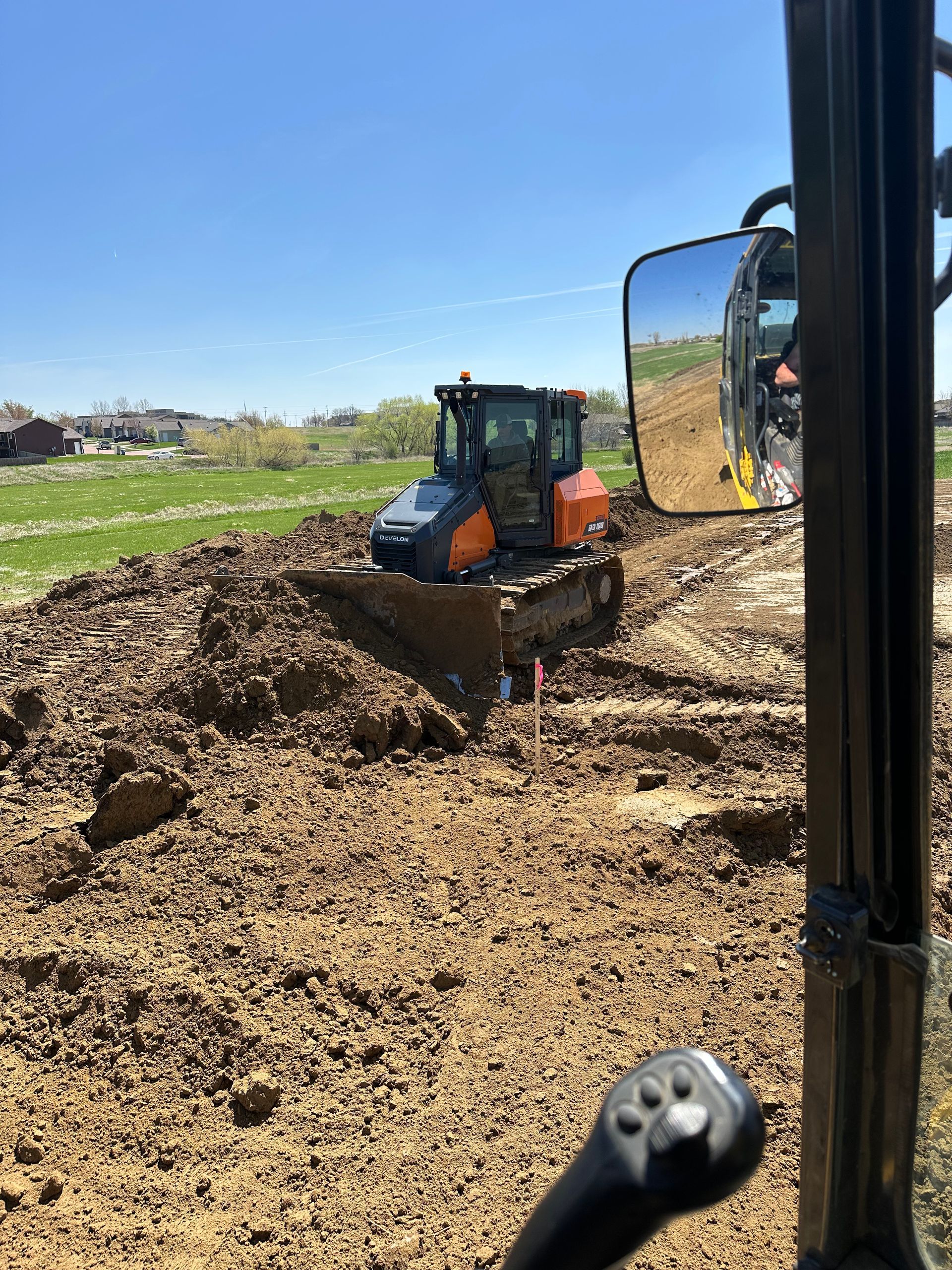 Construction site: Orange tractor excavating dirt on a sunny day. Green field and clear sky in the background.