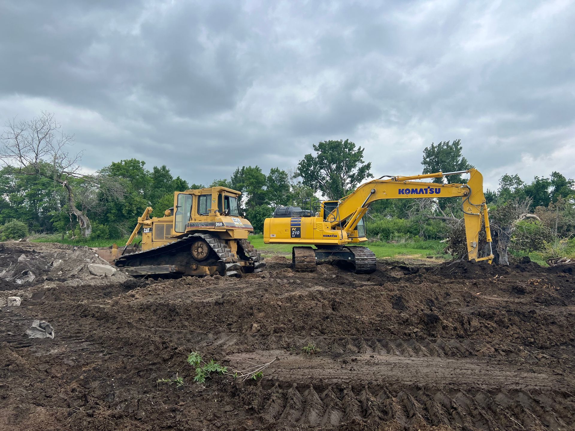 Bulldozer and excavator on a muddy construction site under a cloudy sky.
