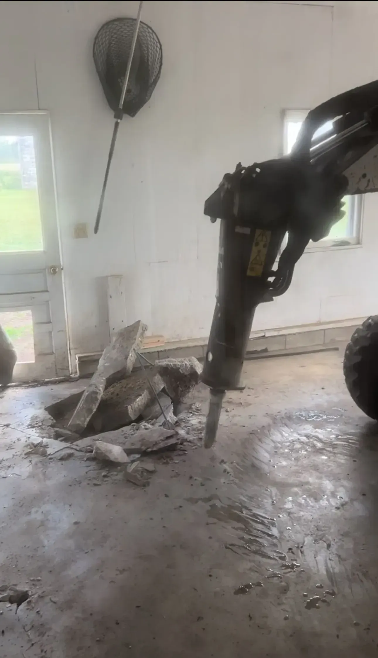 A hammer is breaking a hole in the floor of a garage.