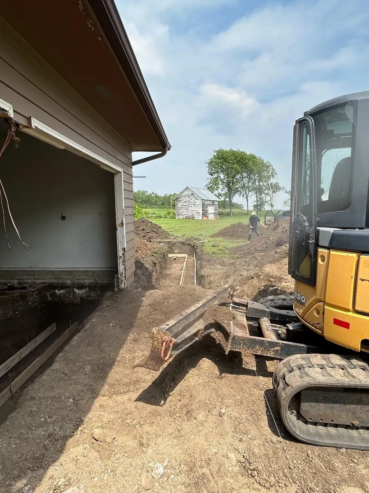 A yellow excavator is sitting in front of a garage.