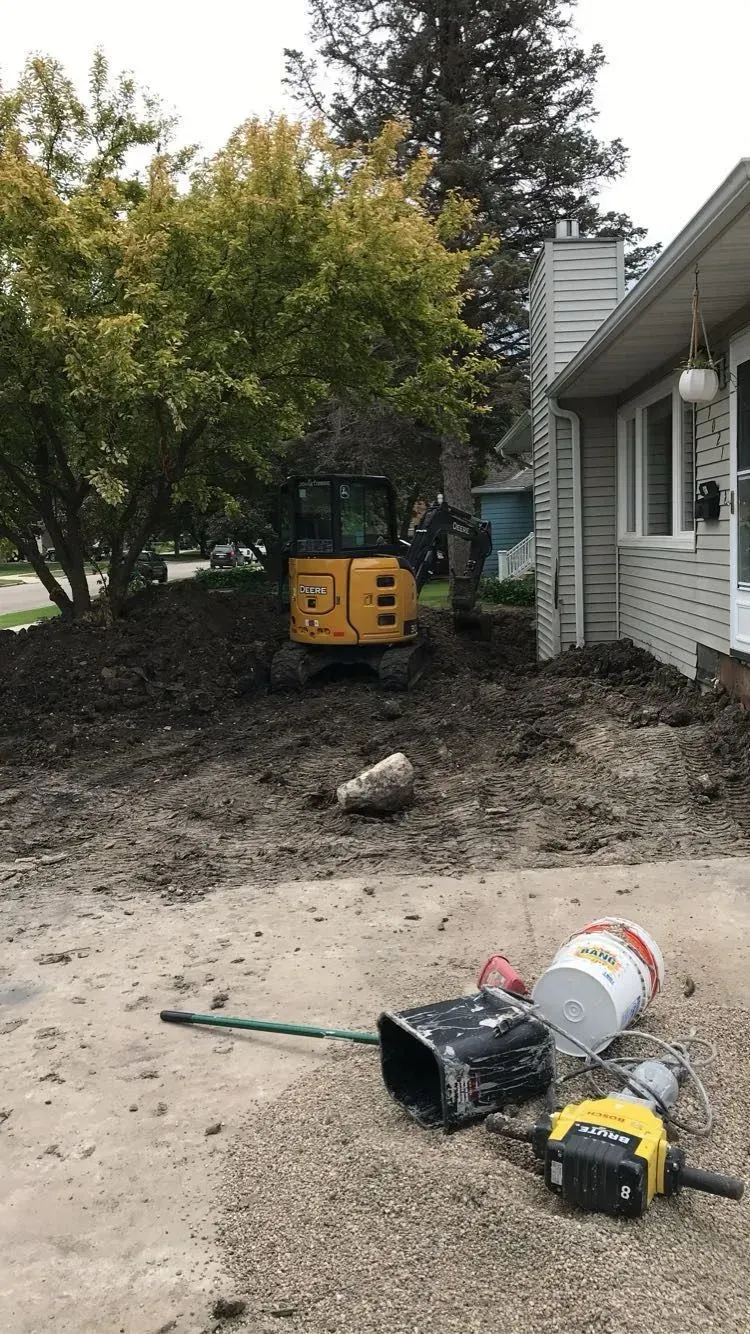 A yellow excavator is sitting in the dirt in front of a house.