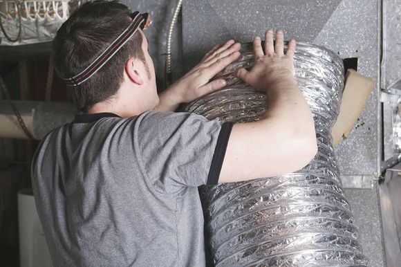 A man is working on an air duct in a room.