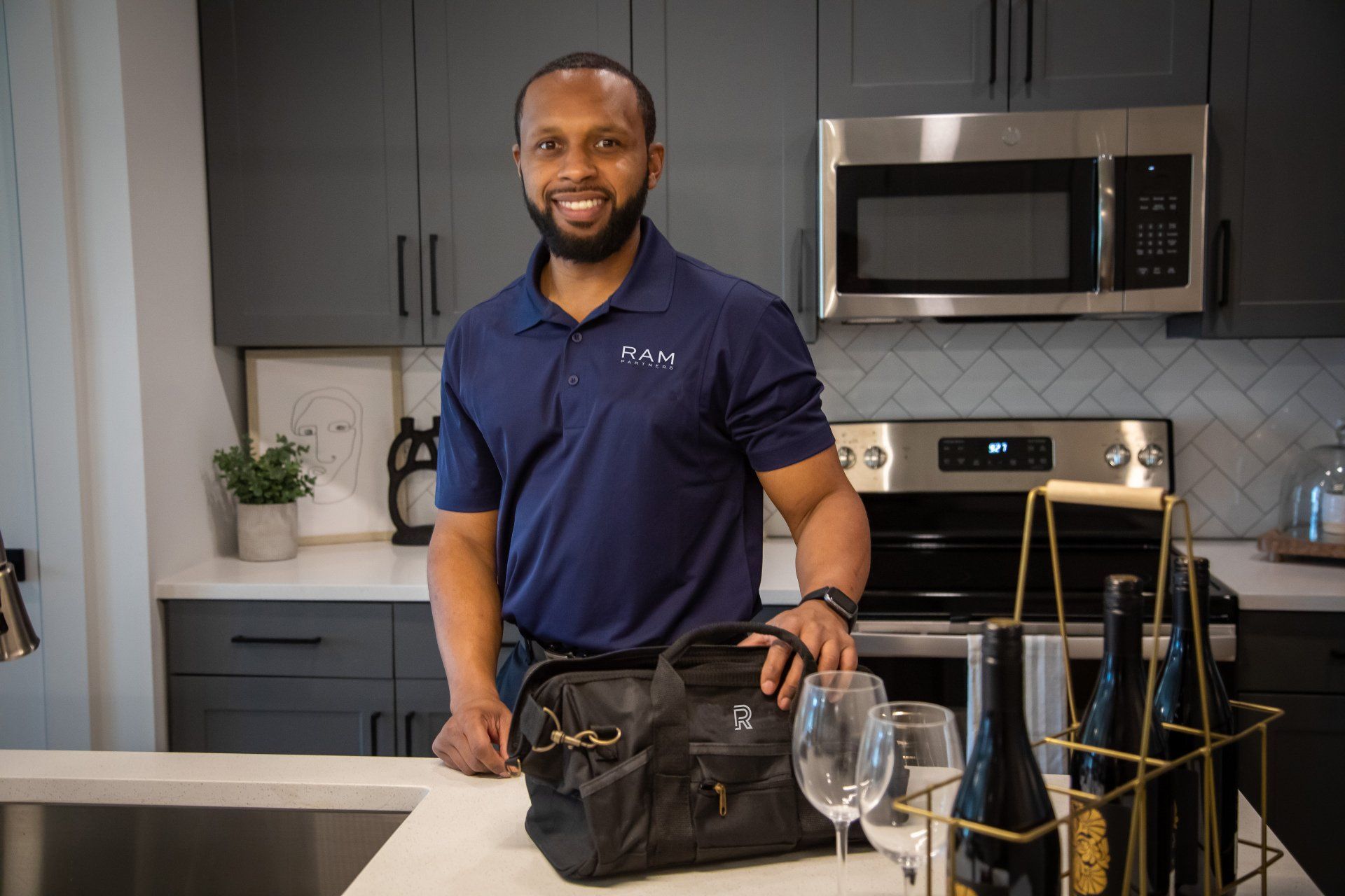A man is standing in a kitchen holding a bag and wine bottles.