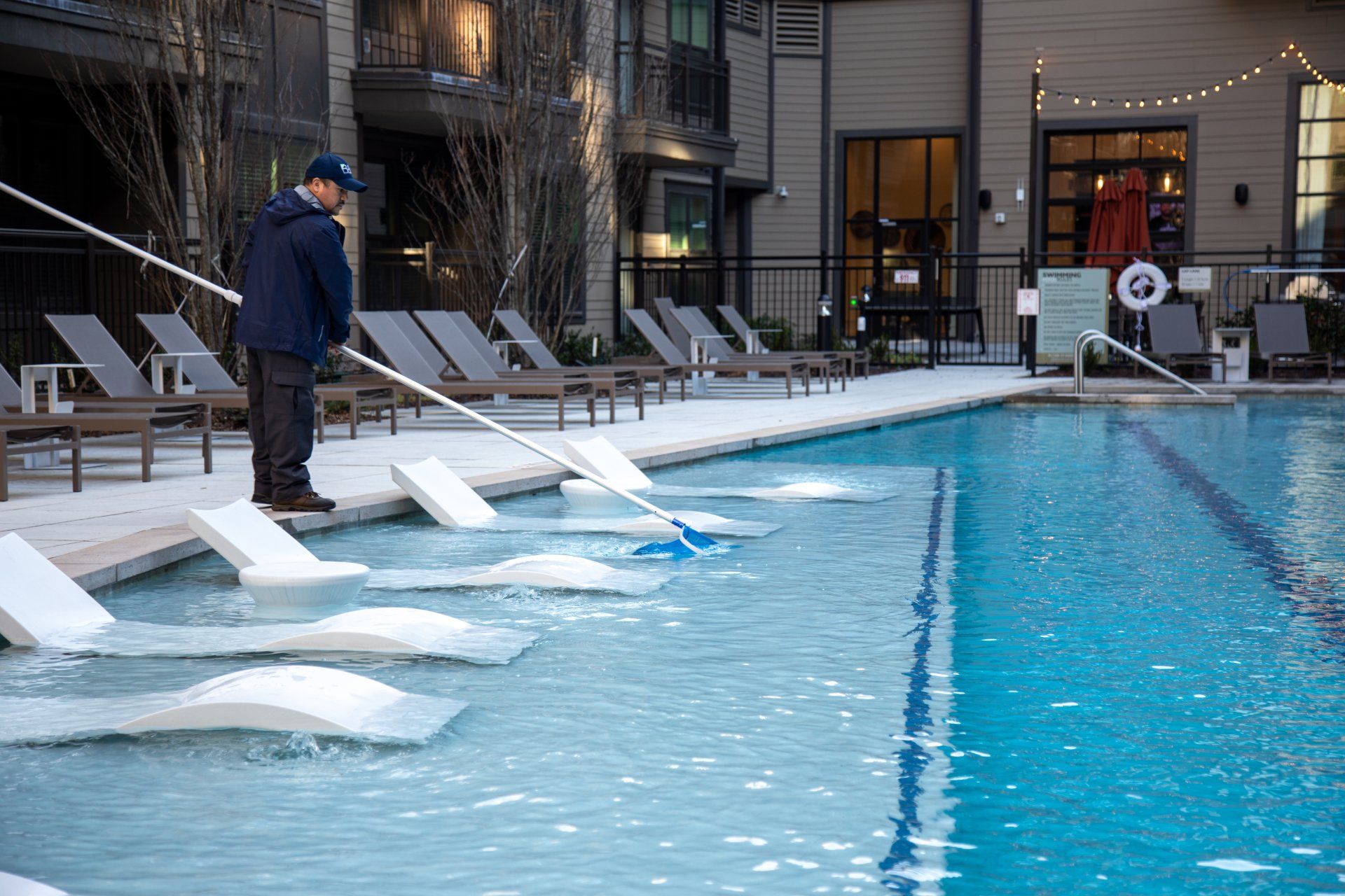 A man is cleaning a swimming pool with a mop.