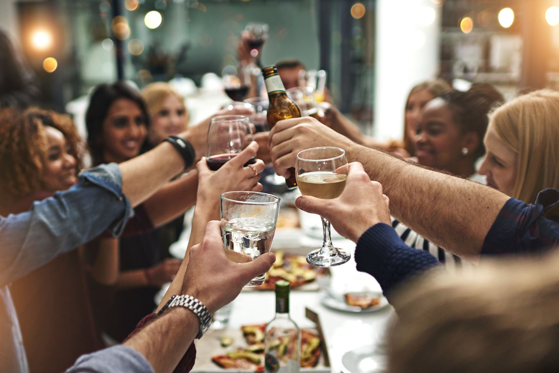 Group of friends toasting drinks at a dinner table, lit by warm lights.