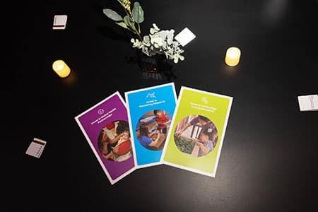 Three brochures are sitting on a table next to a vase of flowers.