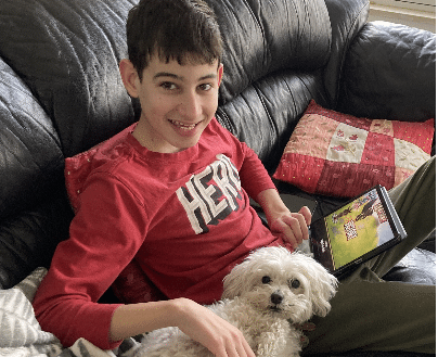A young boy is sitting on a couch with a dog and a tablet.