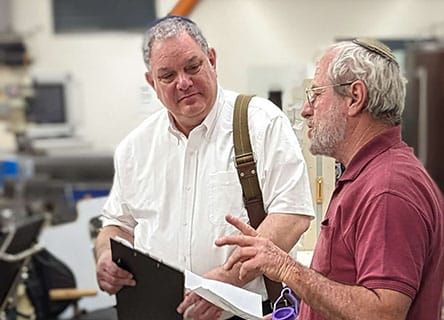 Two men are standing next to each other in a room looking at a clipboard.