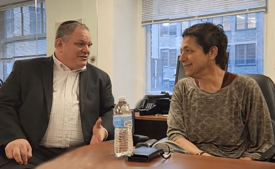 A man and a woman are sitting at a table with a bottle of water on it.