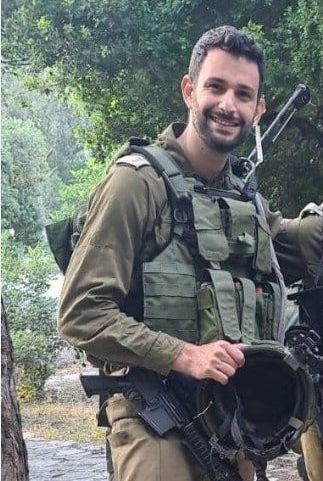 A man in a military uniform is holding a helmet and smiling.