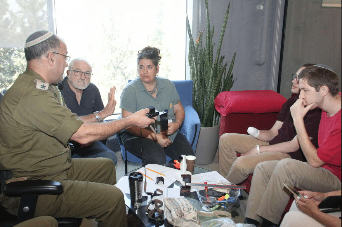 A group of people are sitting around a table talking to a man in a military uniform